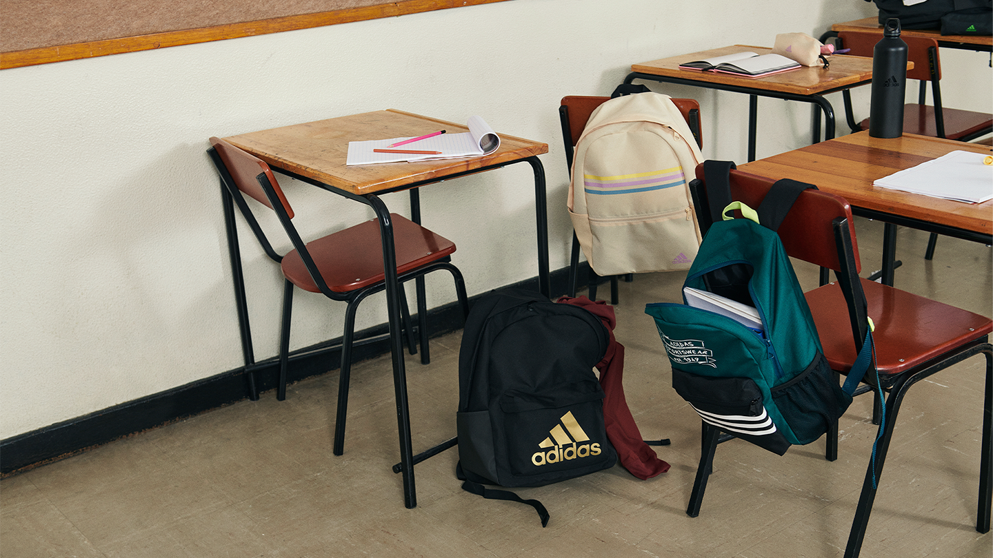 Empty classroom with school backpacks, notebooks, and water bottles on desks and chairs.