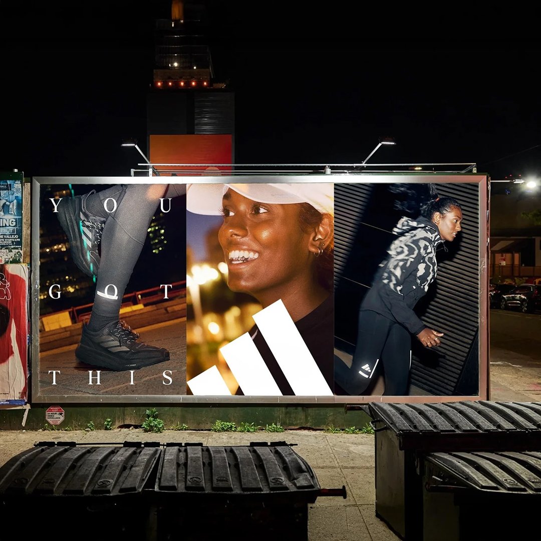 Nighttime billboard advertisement featuring a woman in athletic gear, smiling, with images of a sneaker and a woman running.