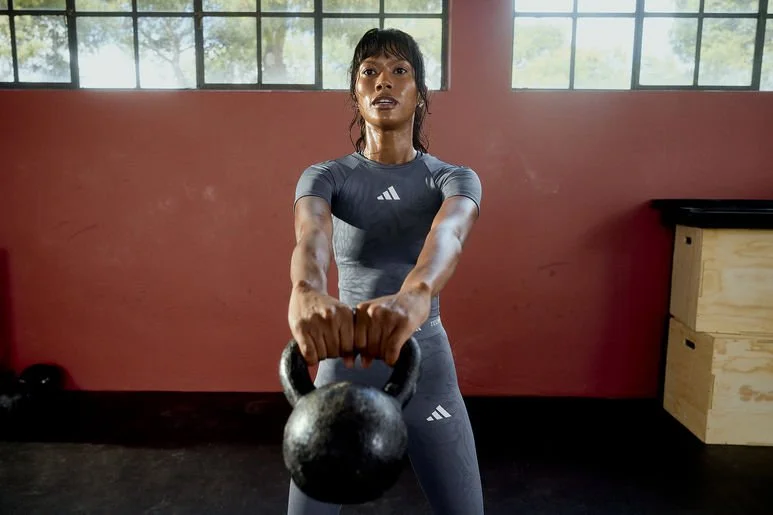 A woman in athletic clothes lifting a kettlebell in a gym.