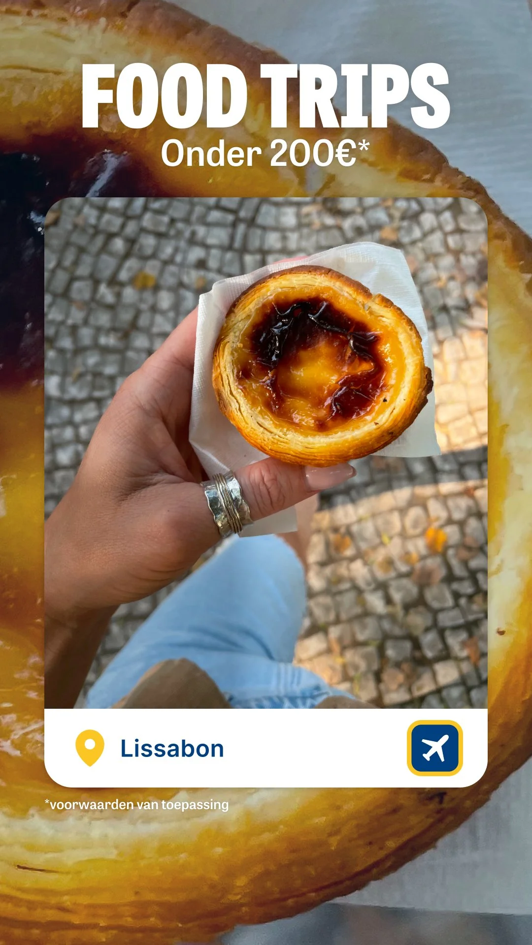 A hand holding a Portuguese egg tart pastry with a flaky crust and sweet custard filling, with a cobblestone street visible underneath.