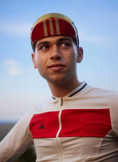 Close-up of a young male cyclist wearing a white and red cycling jersey and a matching red and white helmet, with a clear blue sky in the background.