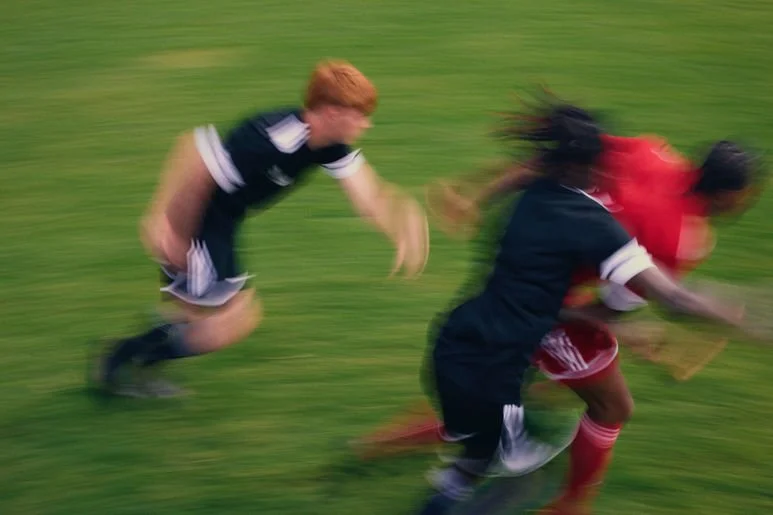 Blurred action shot of children playing soccer on a grassy field, with three kids in focus.