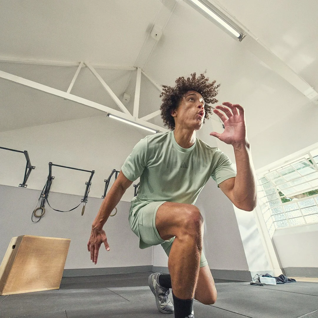 Man in gym wear doing a kneeling exercise in gym with fitness equipment in background.