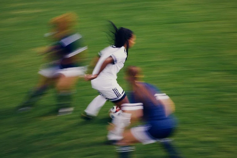 Blurry action shot of a soccer game with players running on a green field.