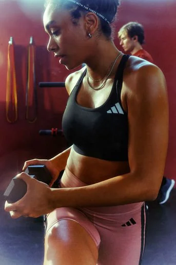 A woman in workout attire checking her phone in a gym setting with gym equipment in the background.