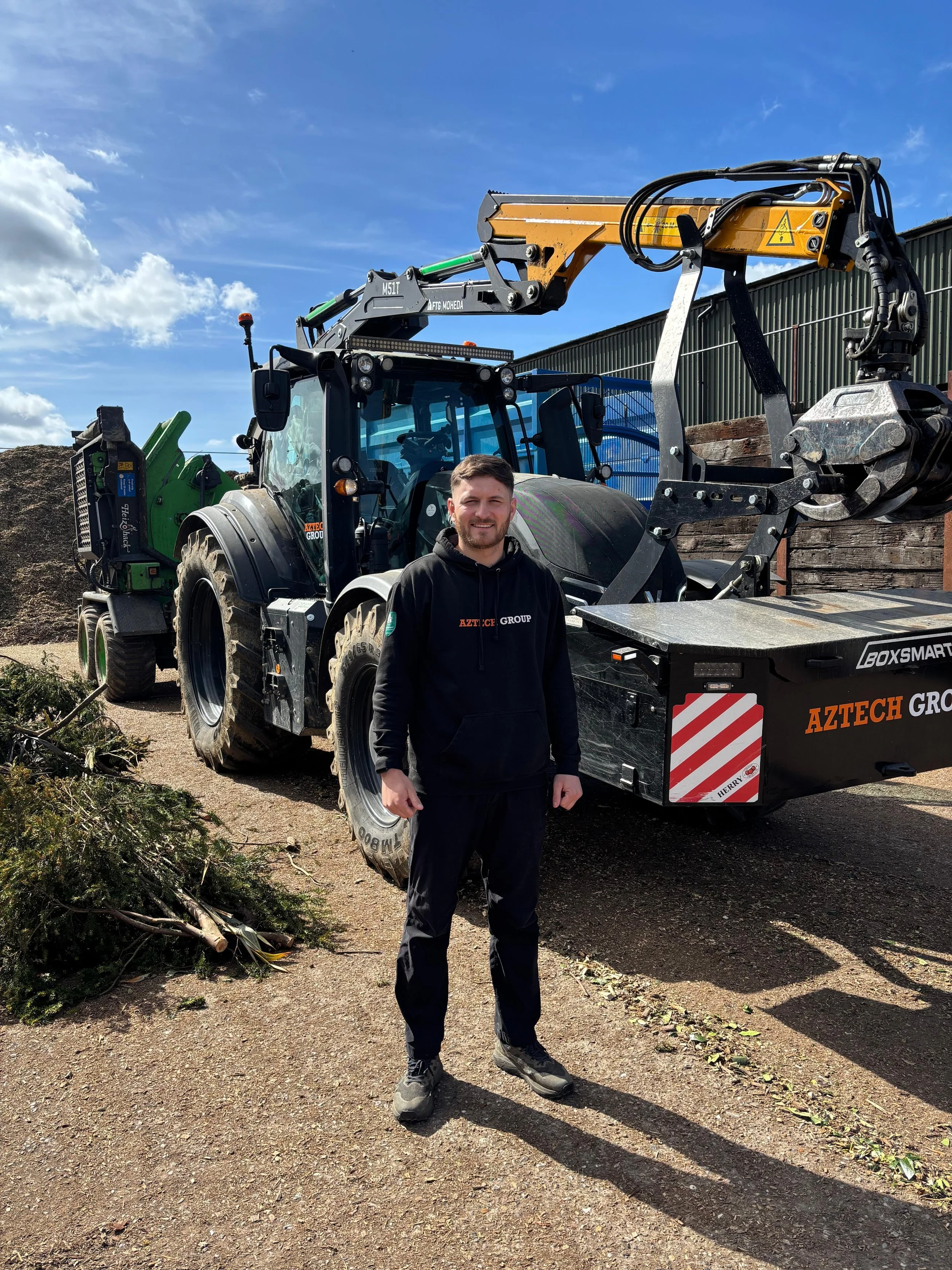 A man standing in front of a large construction vehicle outdoors on a sunny day.