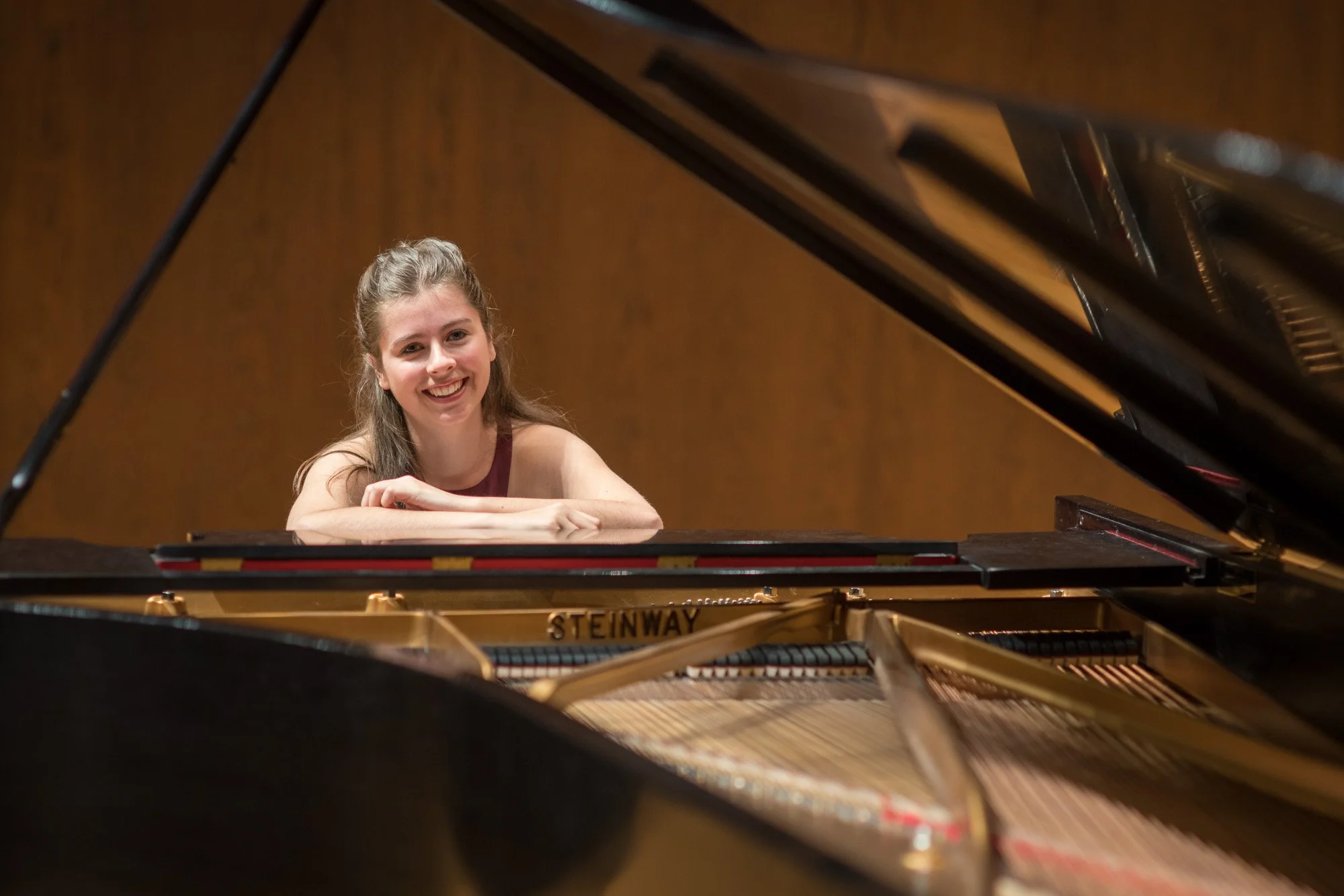 Young woman with long hair smiling at a grand piano in a music room.
