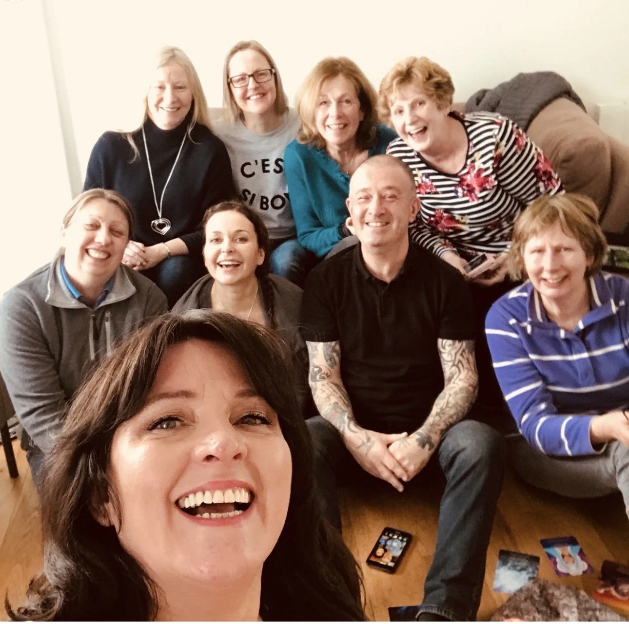 Group photo of nine smiling women and one man gathered in a living room for a get-together.