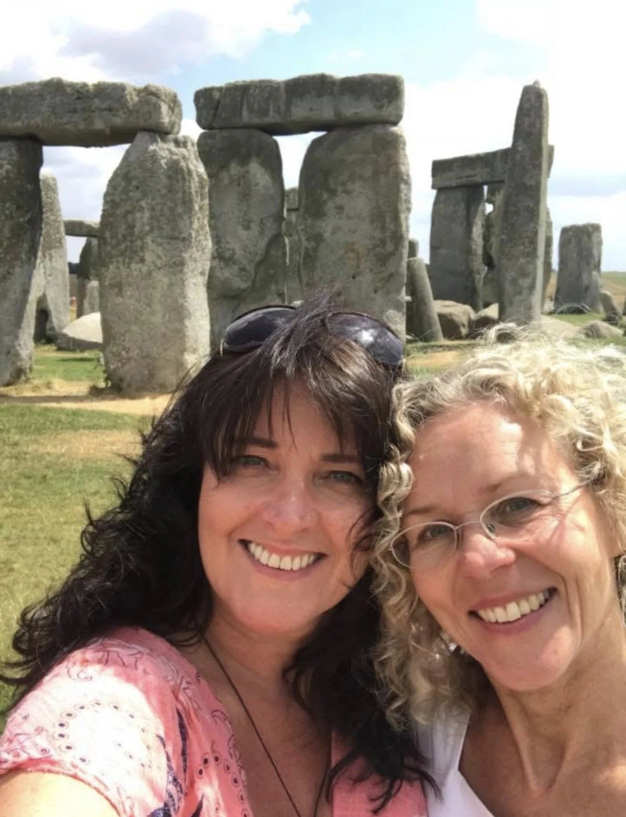 Two women smiling in front of Stonehenge, an ancient stone monument in England.