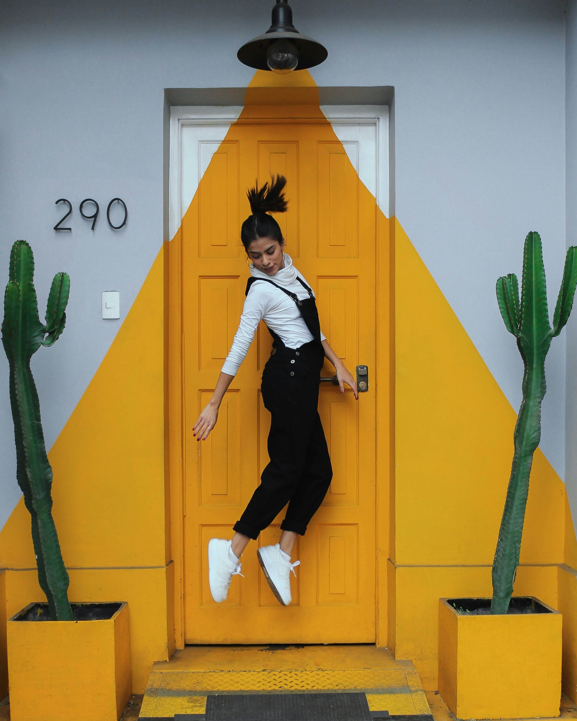 a girl in black outfit and white shoes jumps with yellow/white door in the background