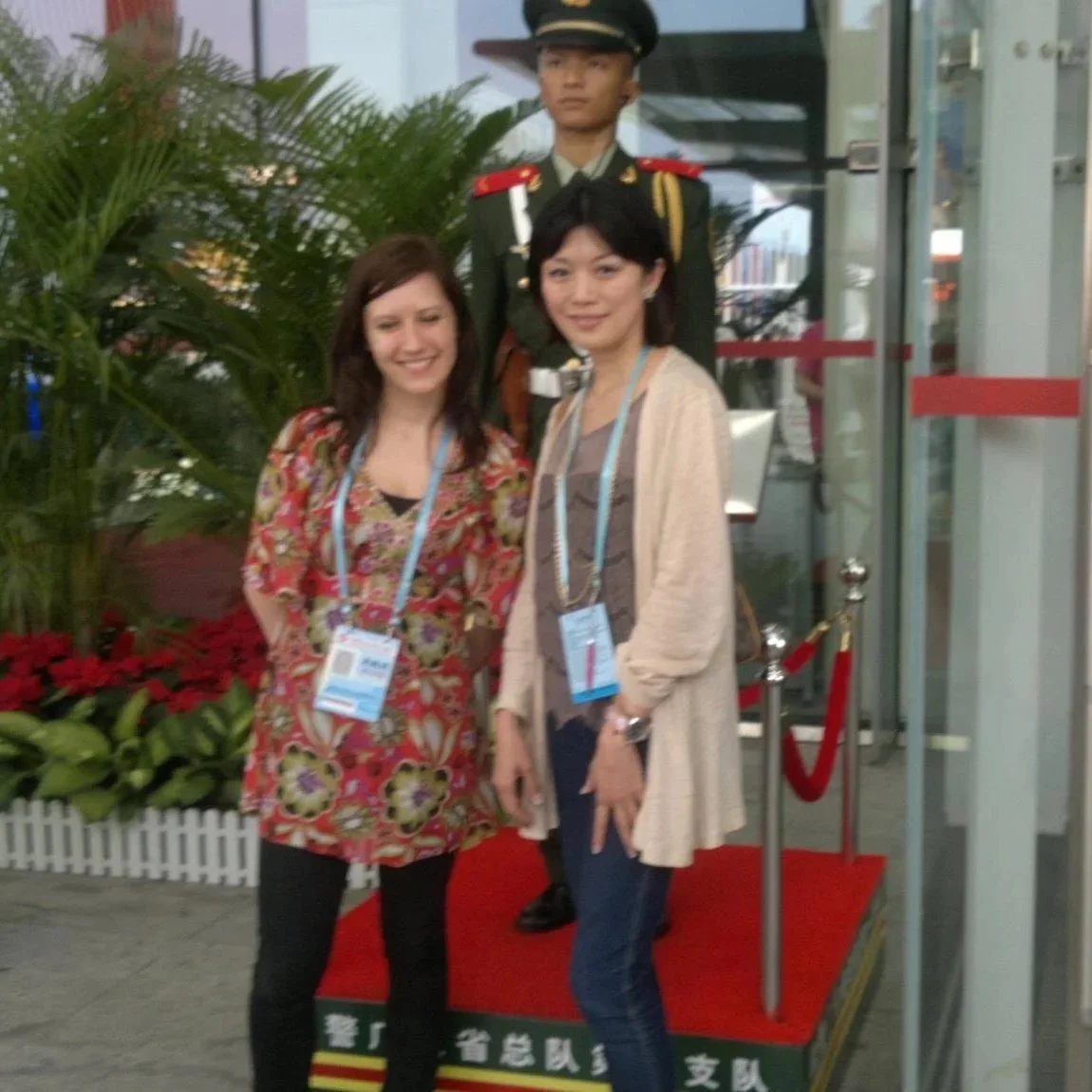 Two women posing for a picture in front of a Chinese Guard at Canton Fair