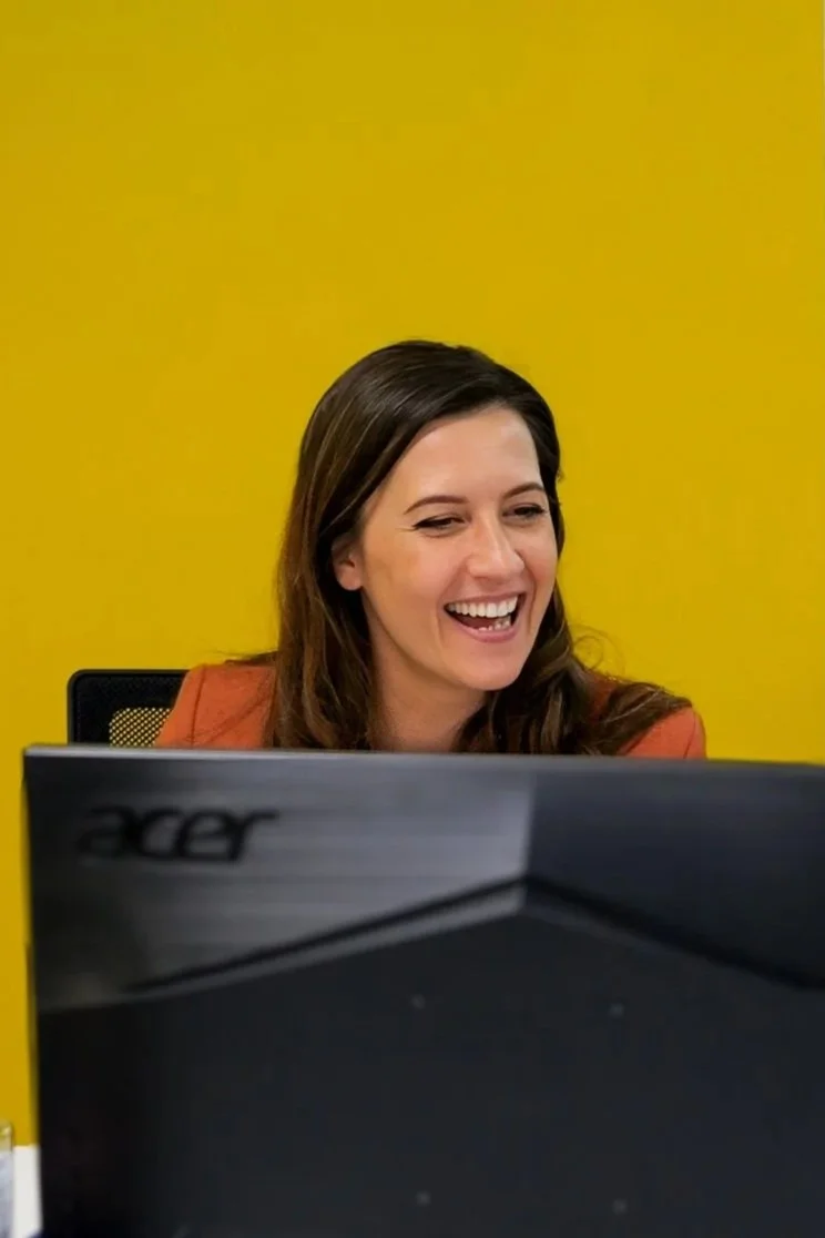 Roza looking at a desk monitor, smiling, symbolising her easy-going and friendly approach to clients,