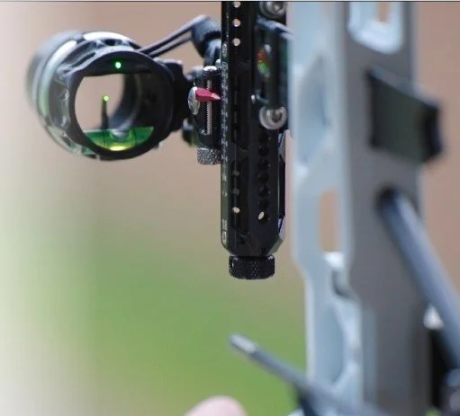 Close-up of a rifle scope mounted on a firearm, with a green reticle visible through the scope lens.