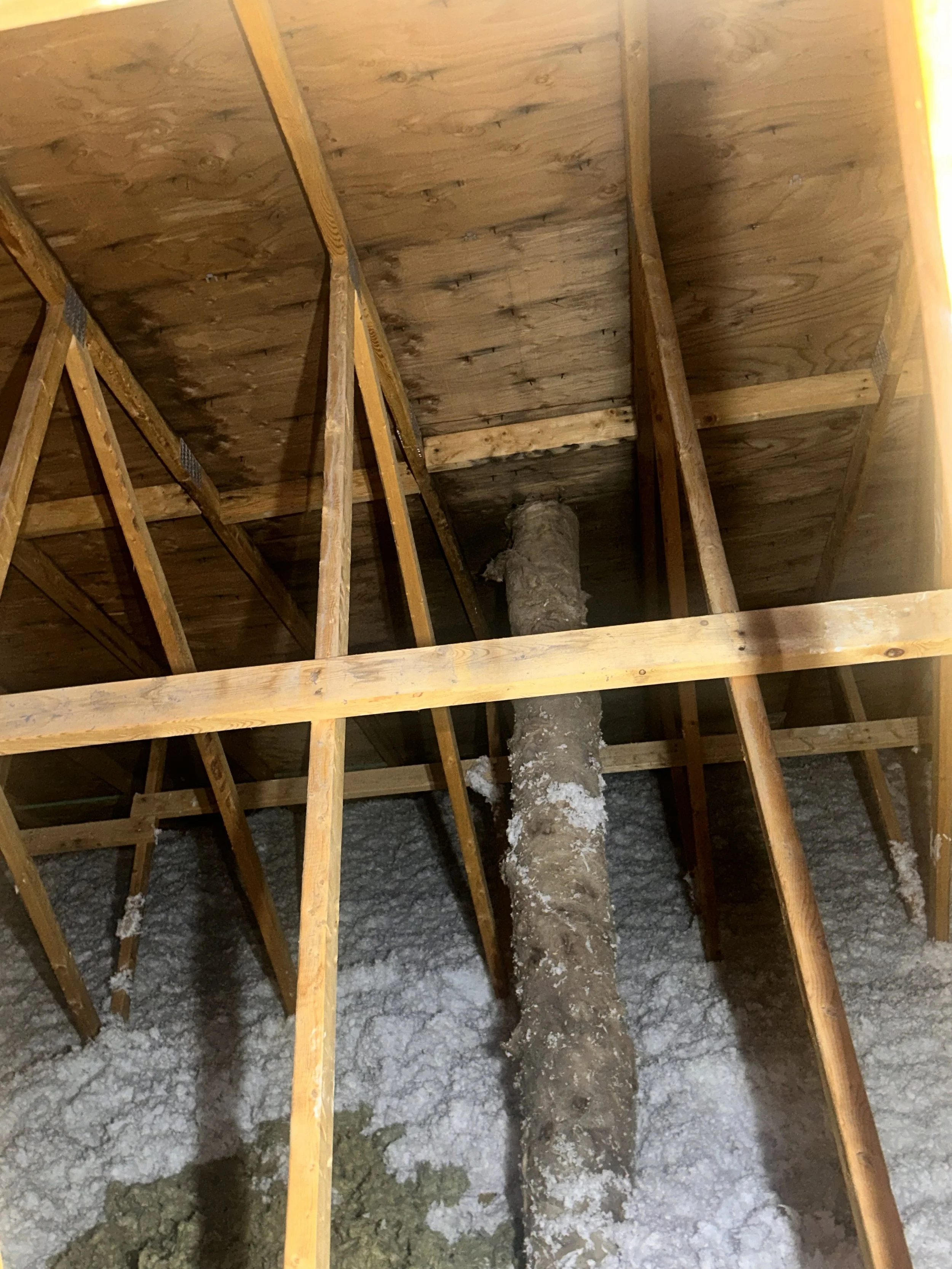 Construction attic with exposed wooden beams, insulation, and a vertical pipe in the center.