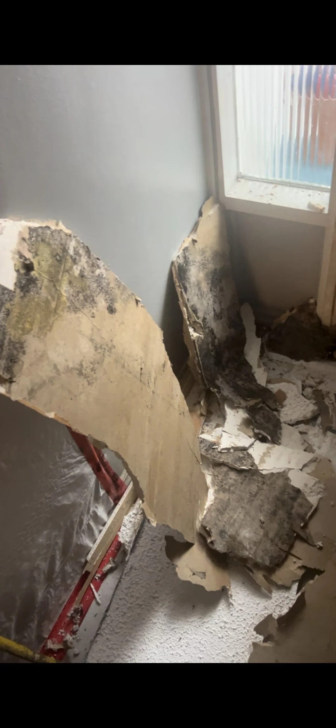 Broken drywall and insulation material from wall repair in a room near a window.