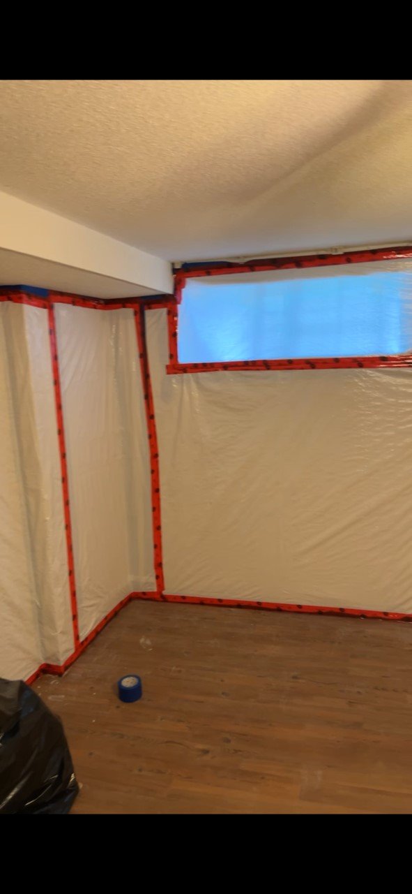Interior room with plastic walls and red painter's tape outlining window and wall edges, indicating renovation work in progress.