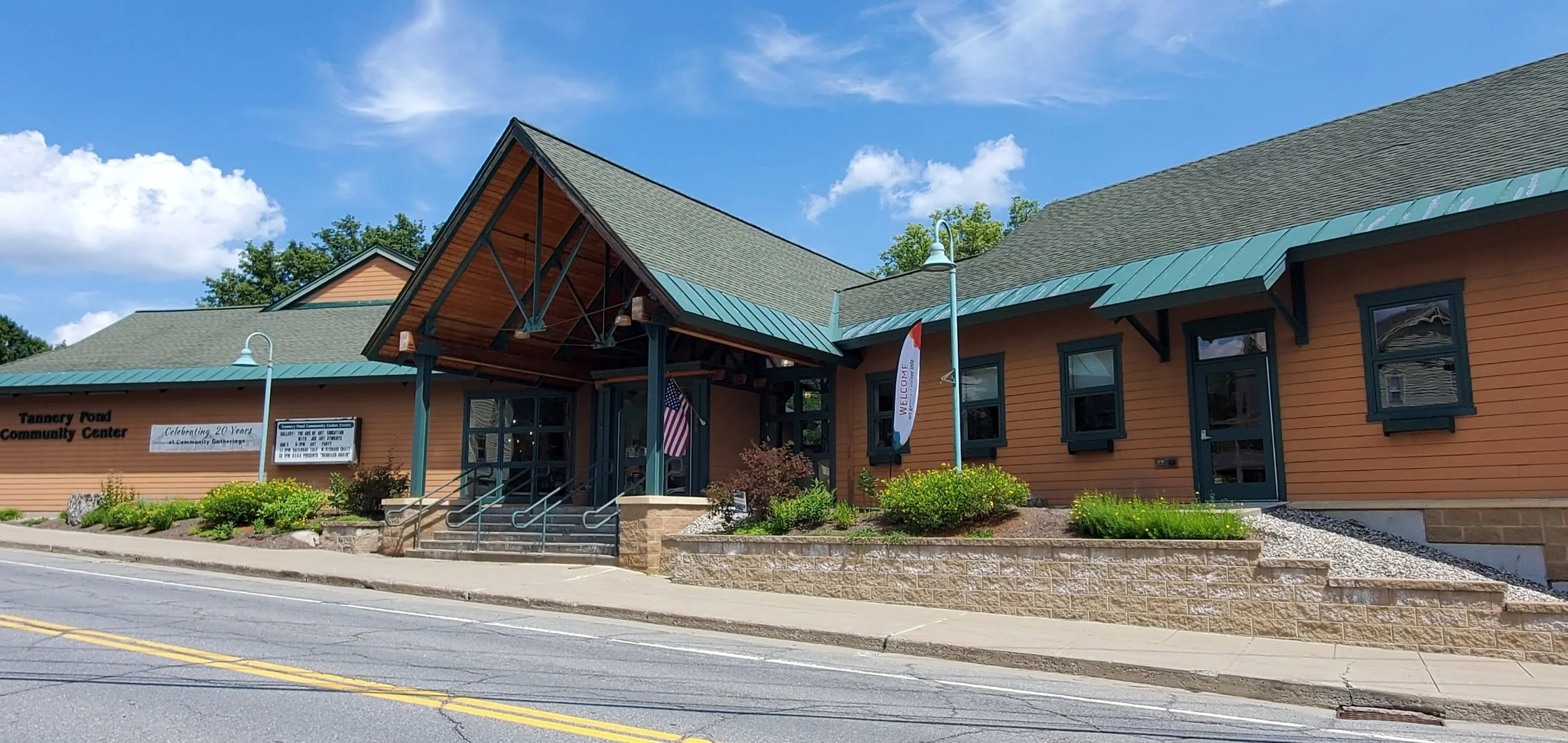 A roadside building with stone retaining walls and green trim and a beautiful vaulted, Adirondack style entrance