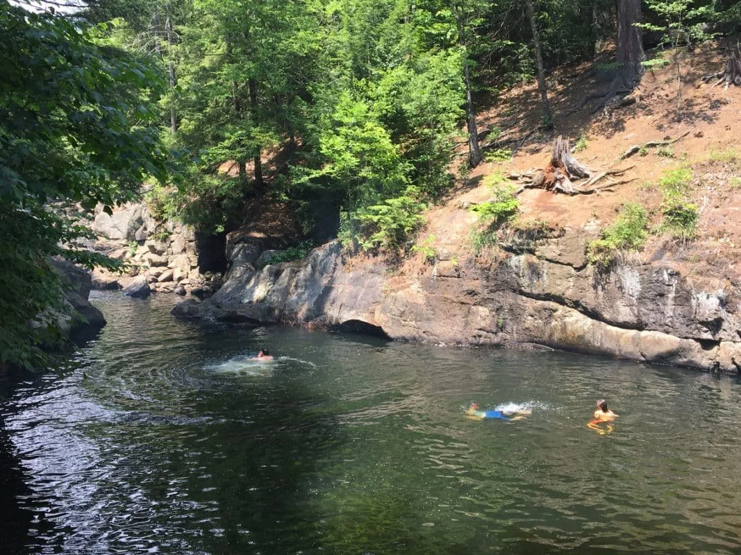 A sunny swimming Hoel with two people treading water and one person kicking while floating on their back.