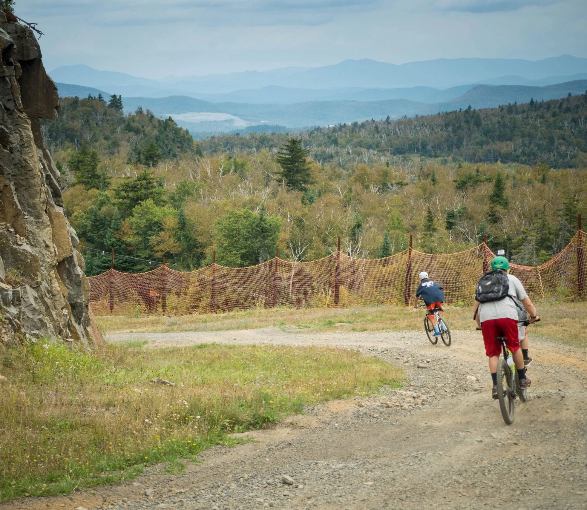 Mountain bikers descend a gravel path with an Adirondack mountain backdrop