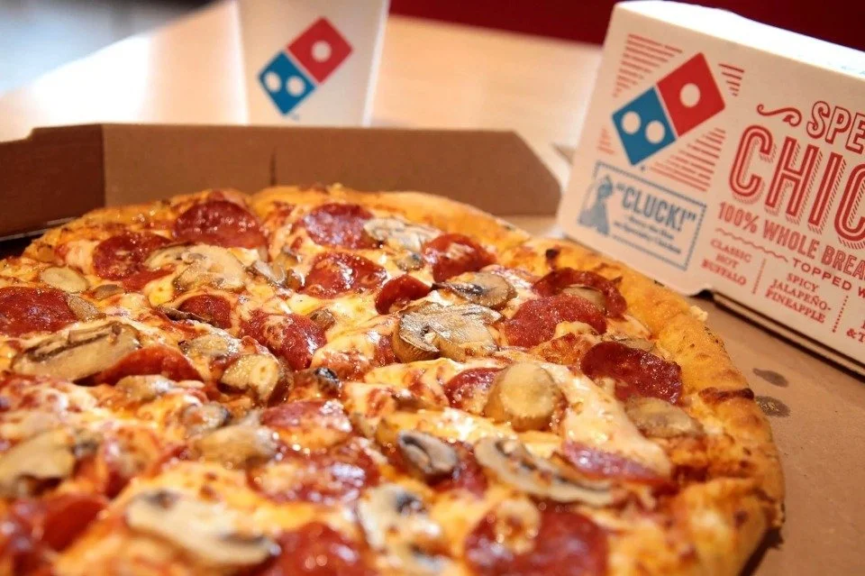 A pepperoni and mushroom pizza in a cardboard pizza box with a Domino's pizza box in the background.