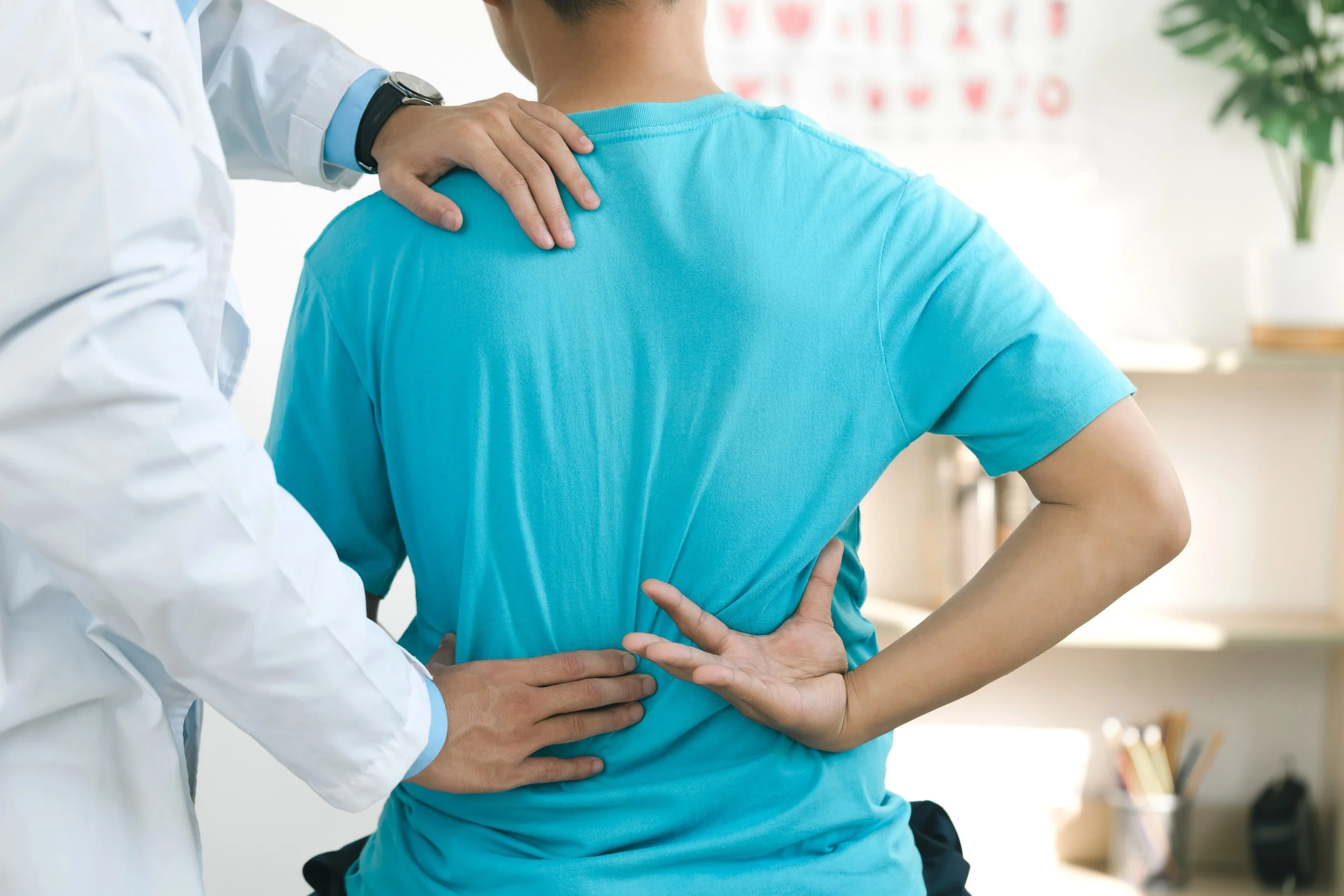 A person in a blue shirt has back pain and is being examined by a healthcare professional.