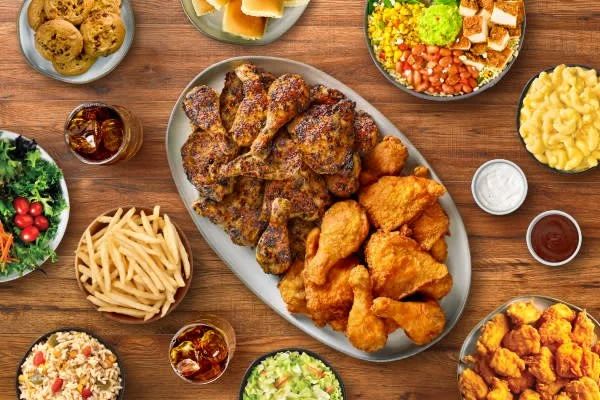 A feast with fried chicken, macaroni and cheese, salad, mashed potatoes, and various sides on a wooden table.