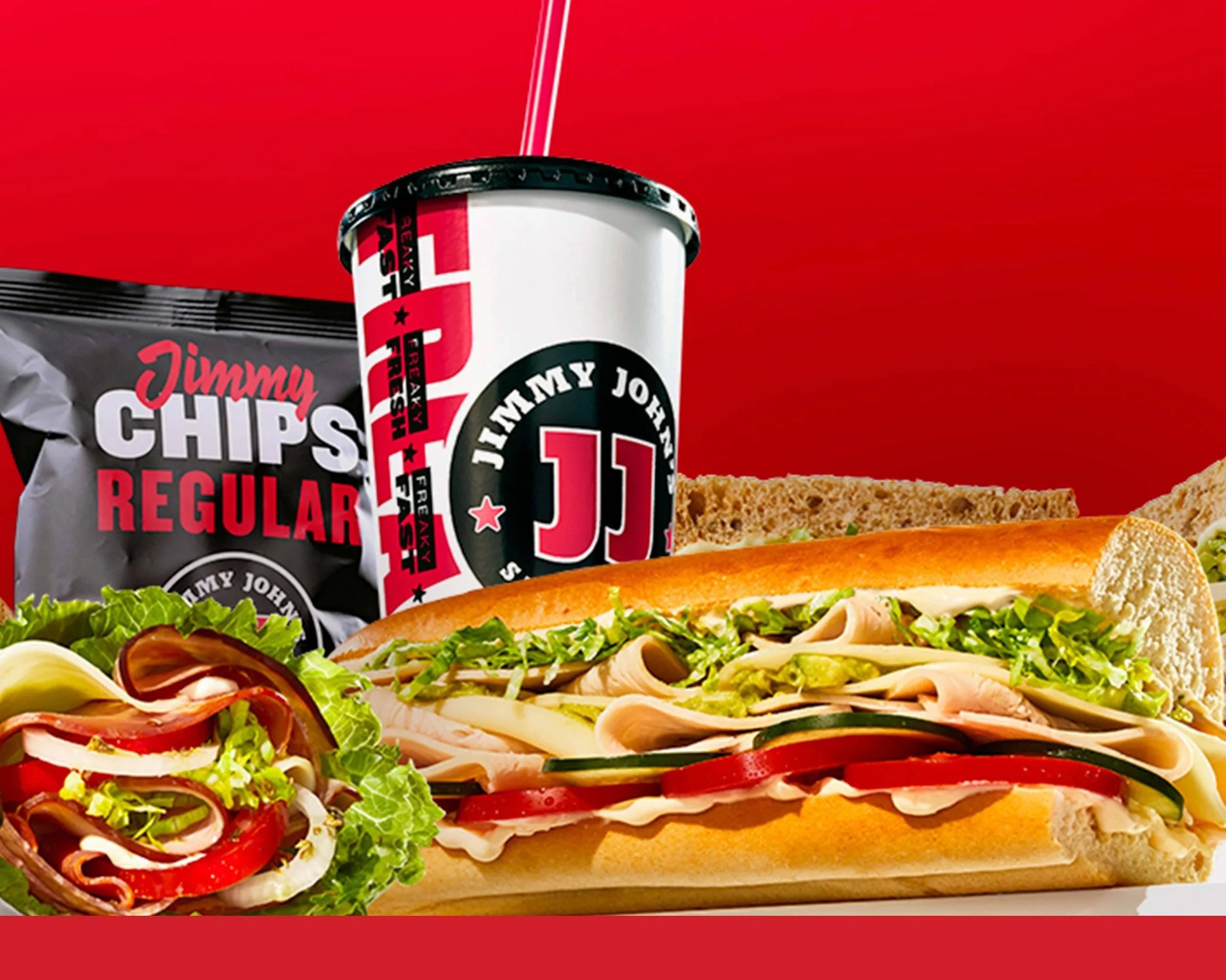 Sub sandwich with lettuce, tomato, turkey, cucumbers, and mayonnaise, with a side salad, potato chips, and a soda in a red background.