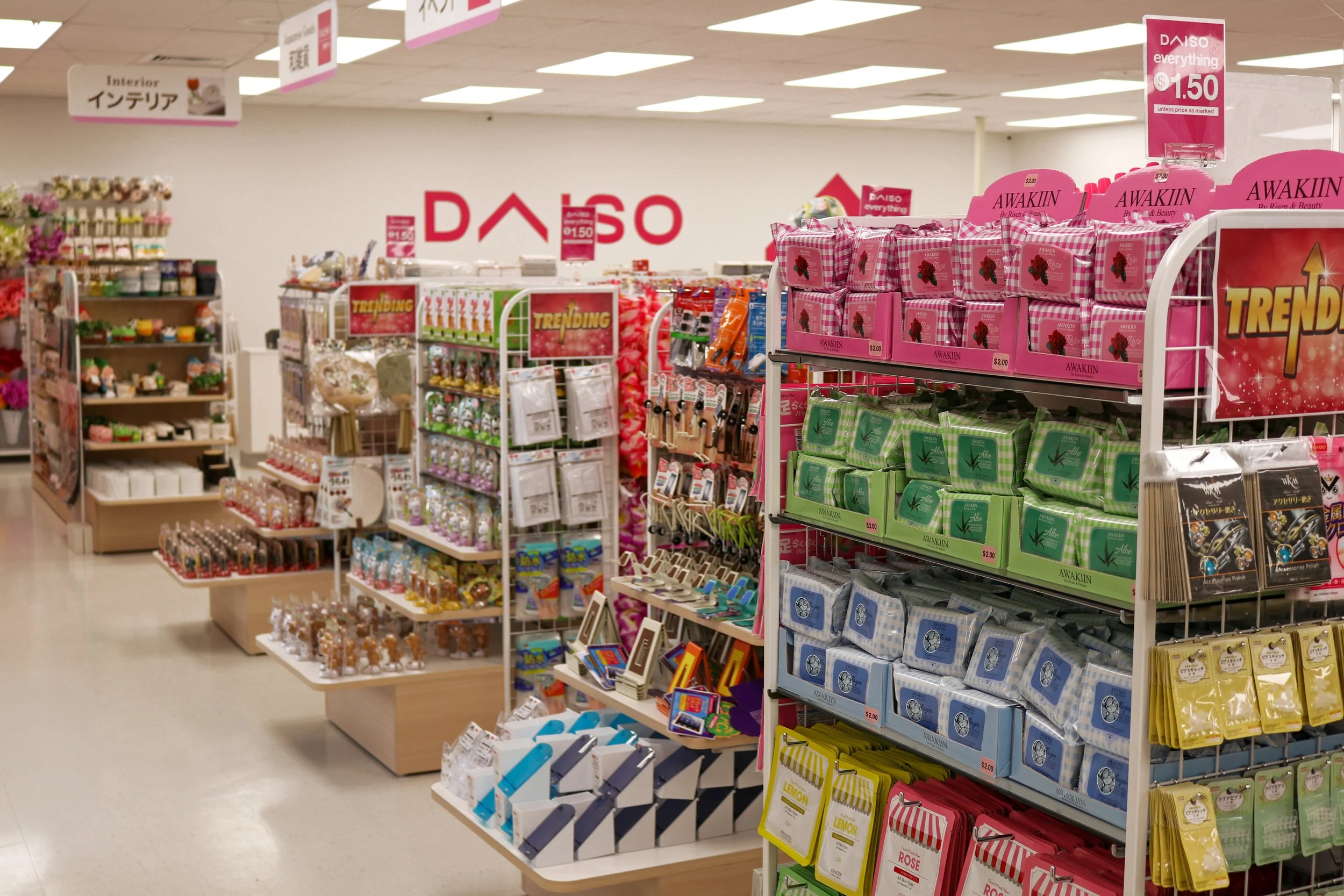 Inside a Daiso store with shelves stocked with colorful household and gift items, including soaps, candles, and accessories, with signs showing prices and store branding.