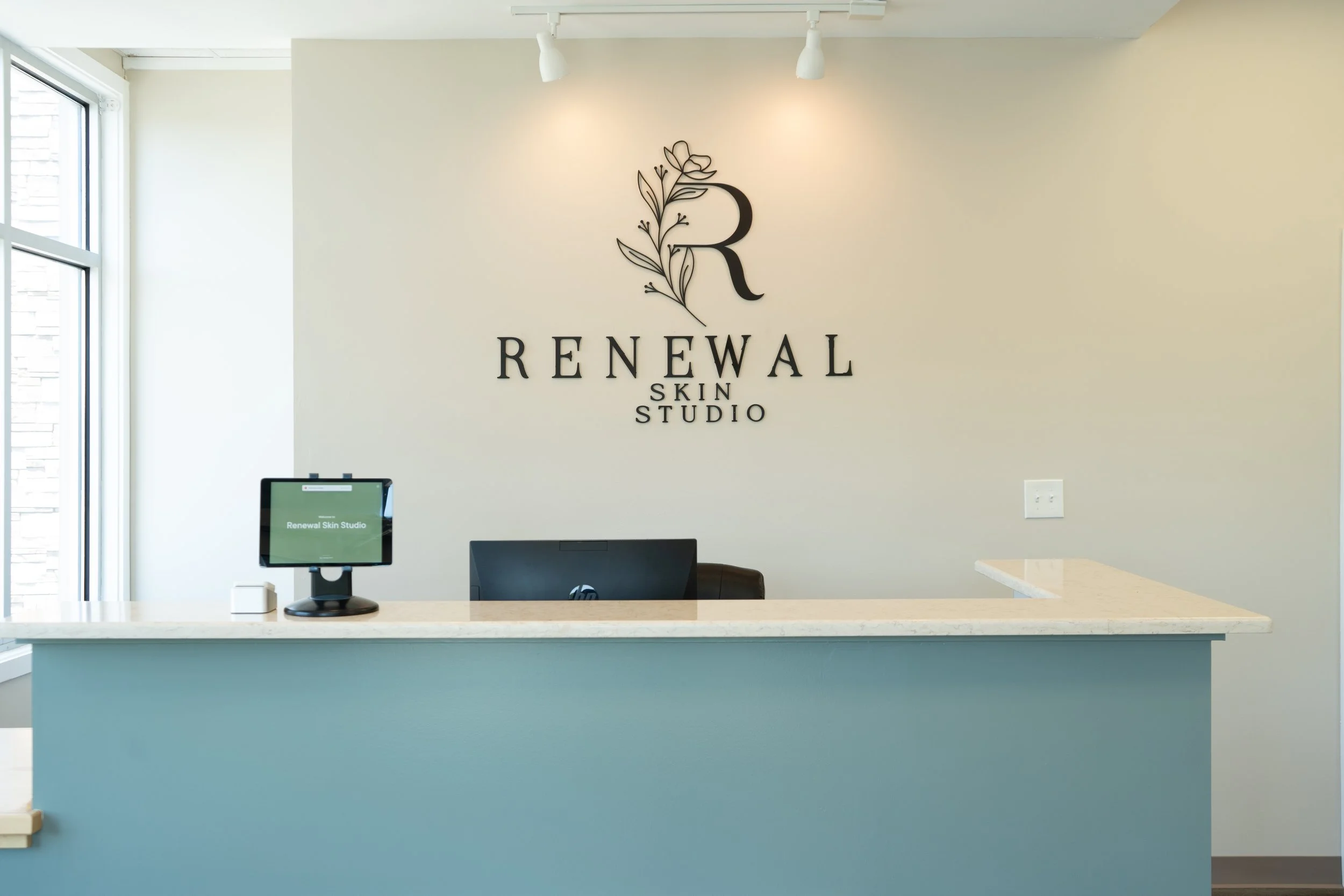 Interior of a skincare studio reception area with a sign reading 'Renewal Skin Studio' and a reception desk with a computer.