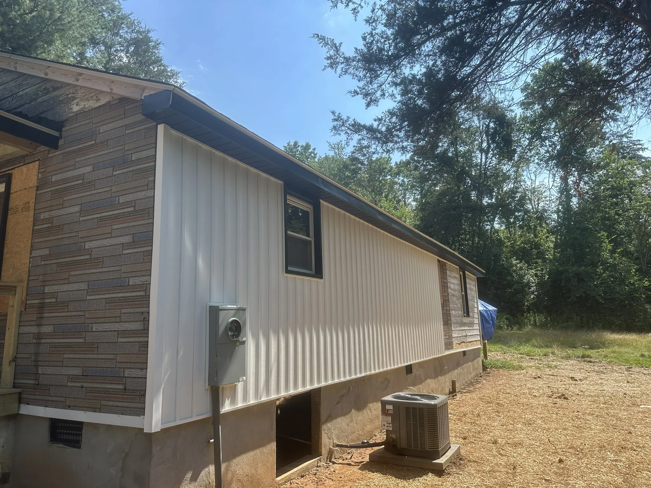 Side view of a residential house under construction showing exterior wall with brick and siding, window, and HVAC unit outside.