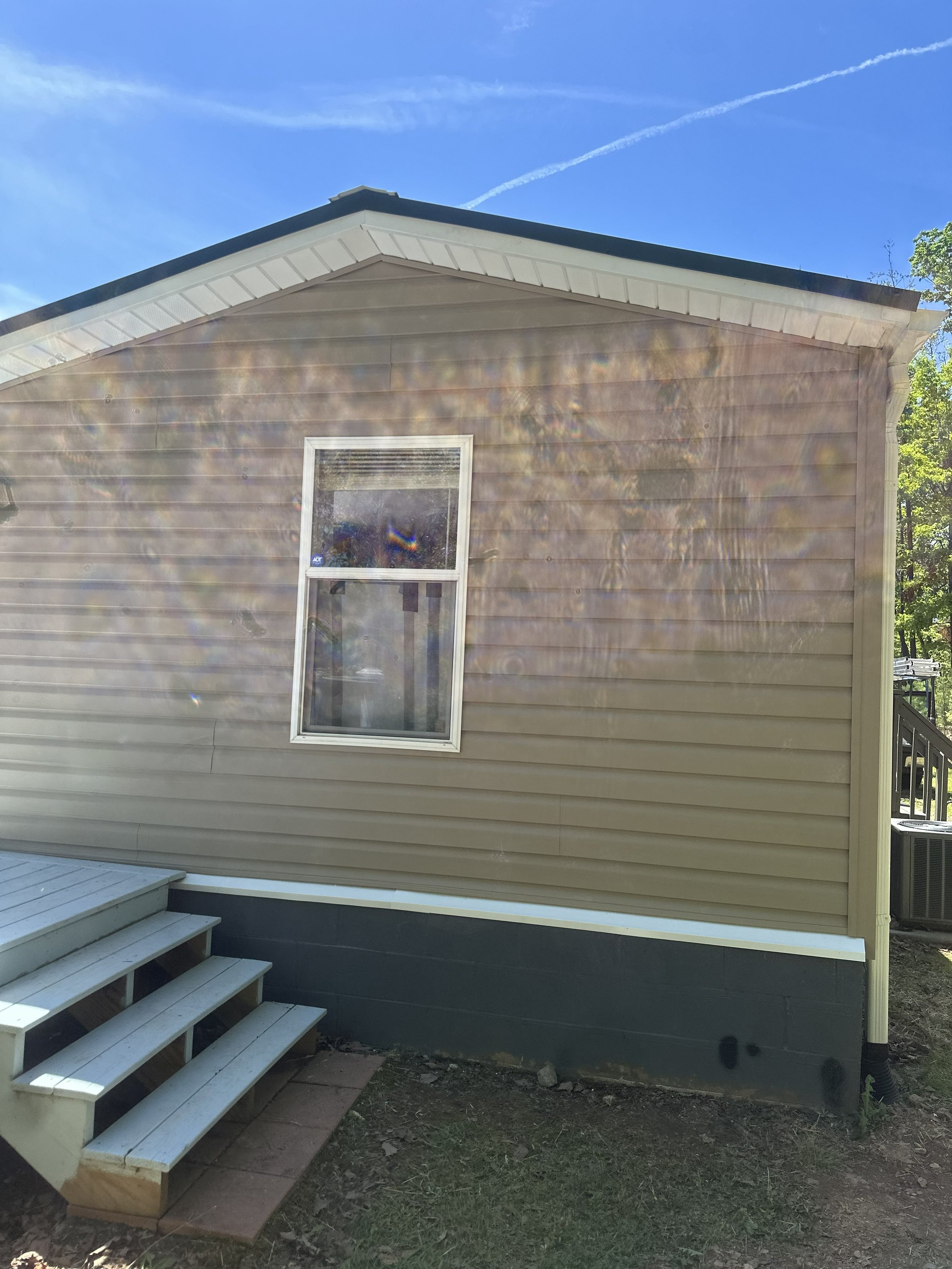 New beige house with siding, a single window, and a small wooden staircase outside.
