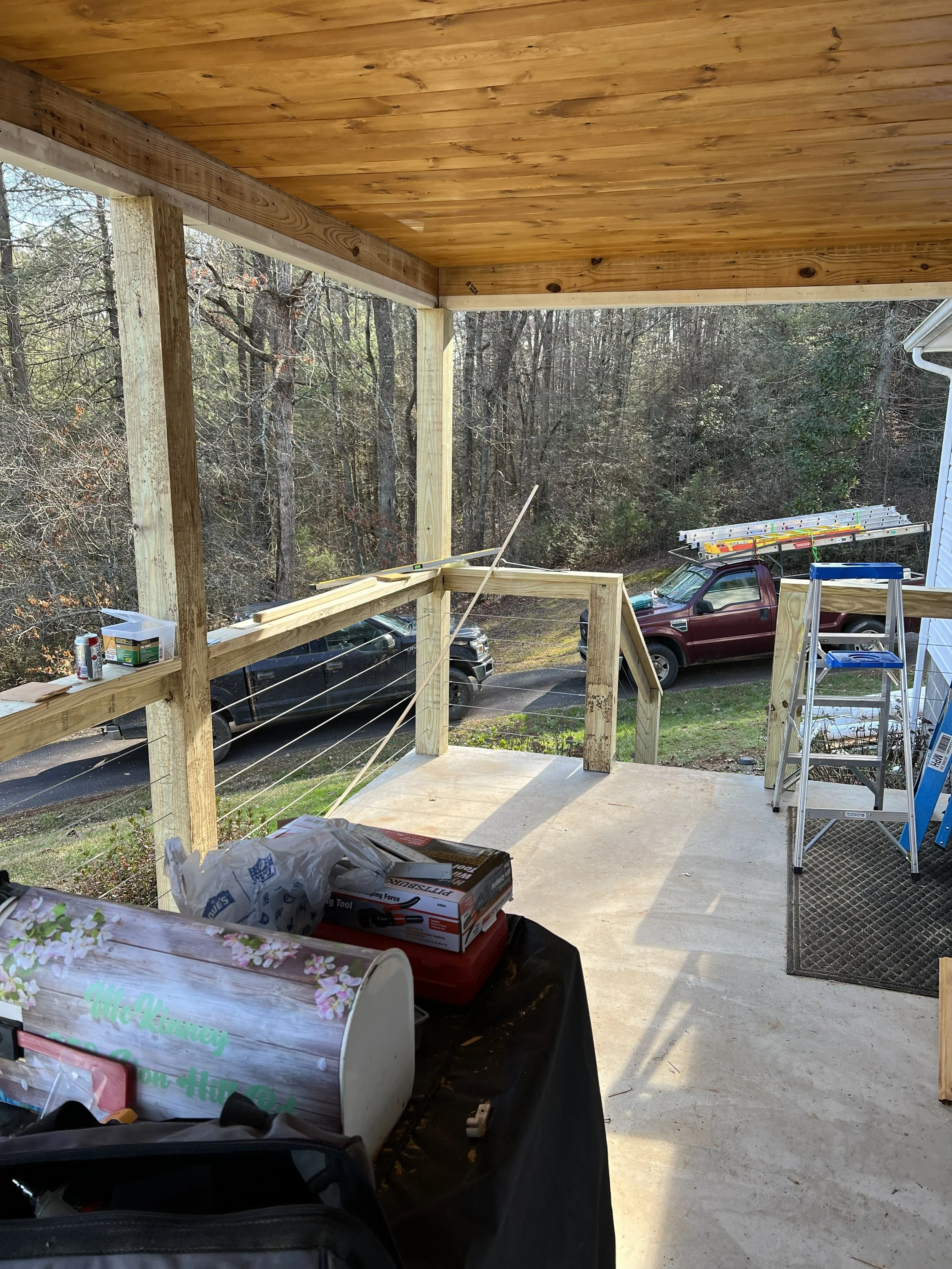 Construction site with wooden porch under construction, vehicles parked nearby, tools, and supplies on a table.
