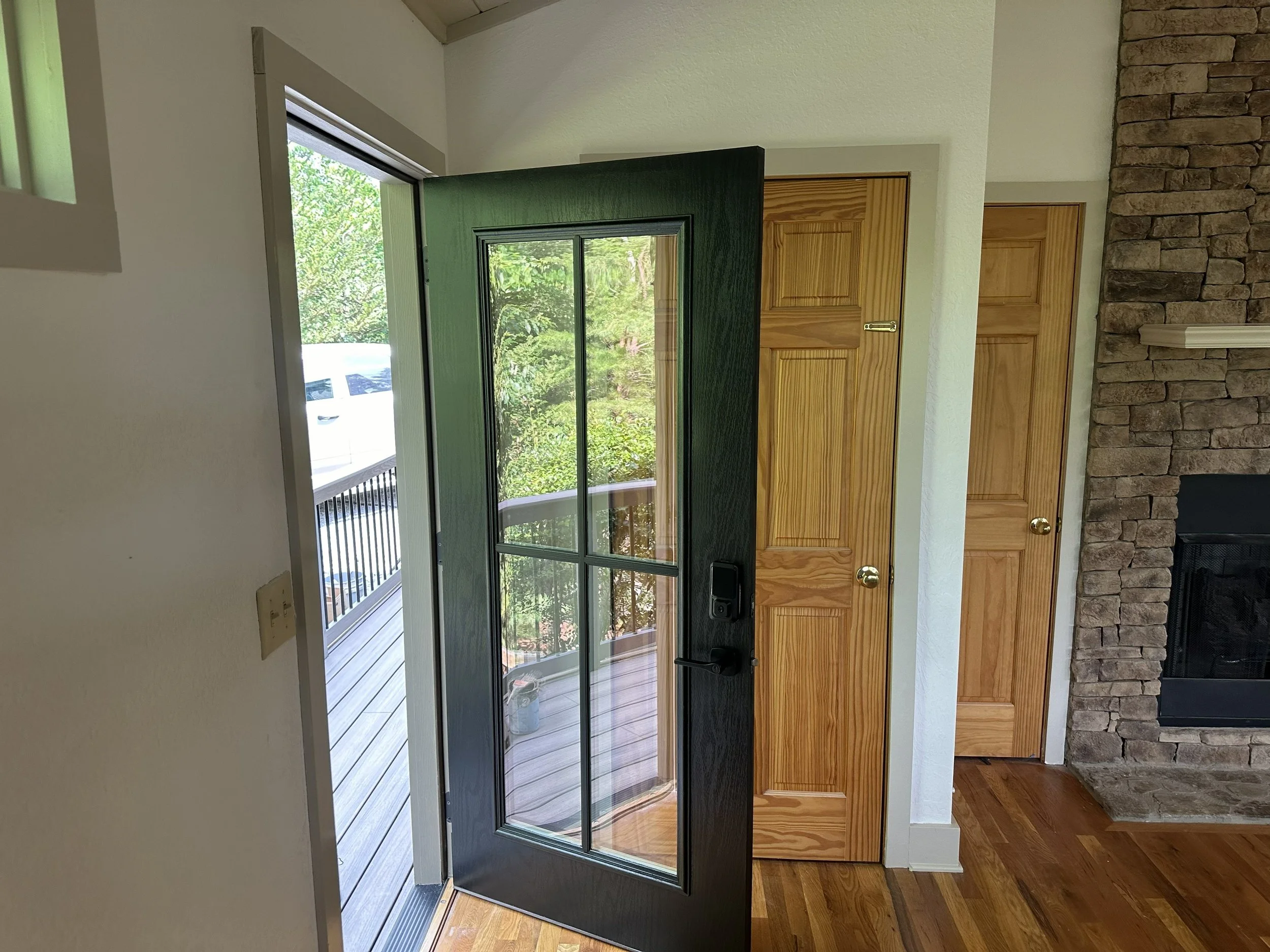 Open black window screen door leading to a deck with trees visible outside, indoors with wooden doors and a brick fireplace.