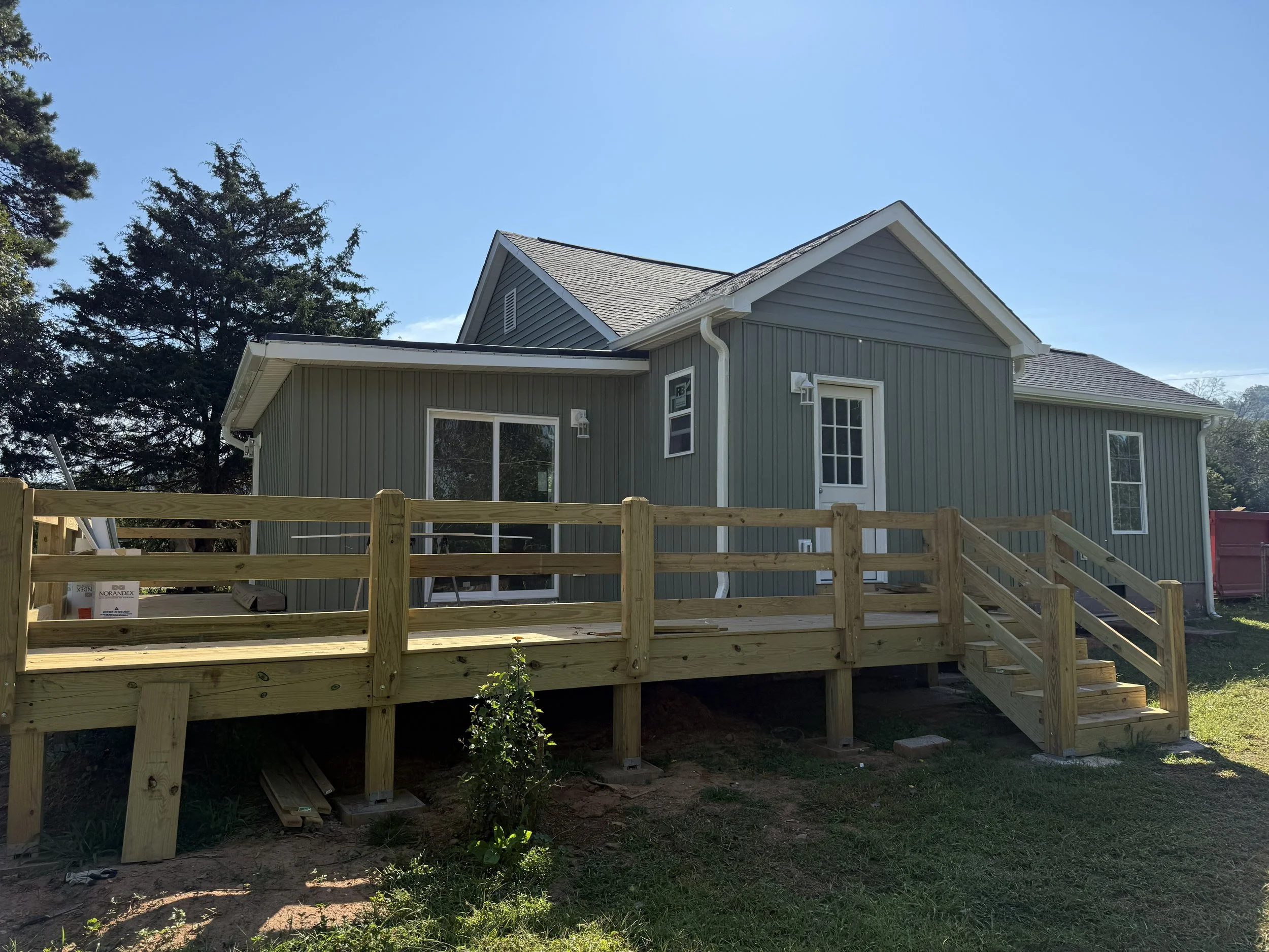 Backyard of a house under construction with a wooden deck and railing, and trees in the background.