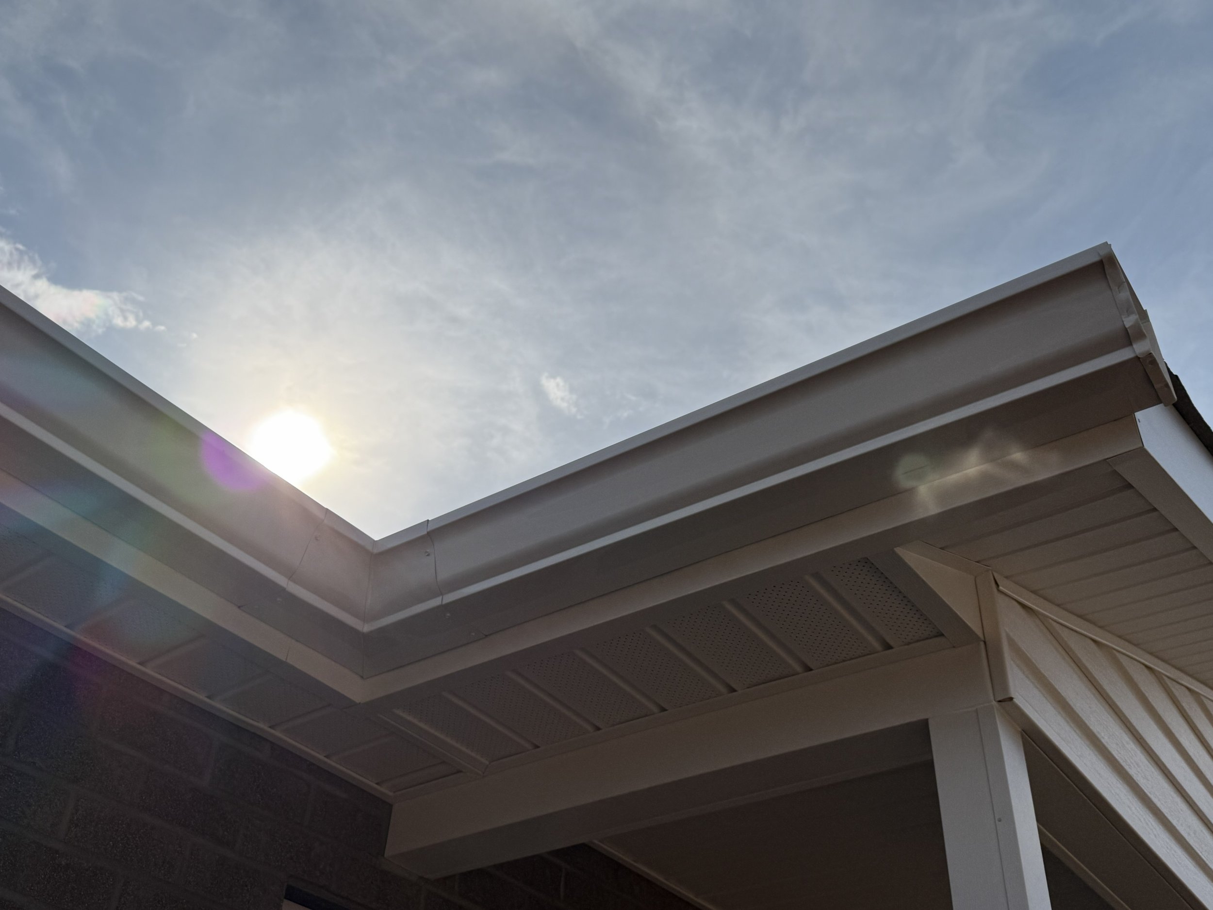 A view of the sky through a roof opening, with part of a building's roof visible in the foreground.