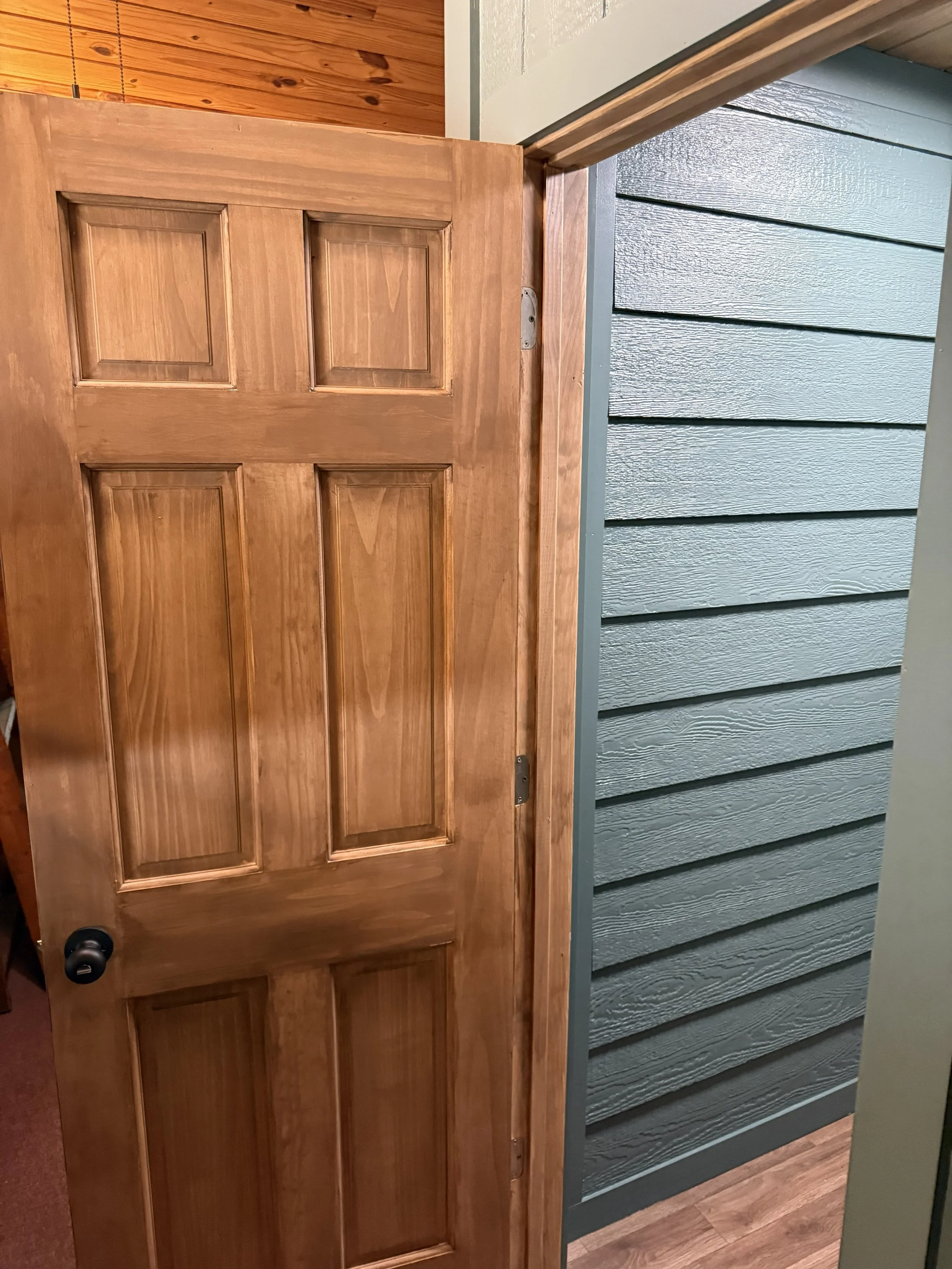 A wooden door with a black handle in a room with wooden and blue siding walls and a wood floor.
