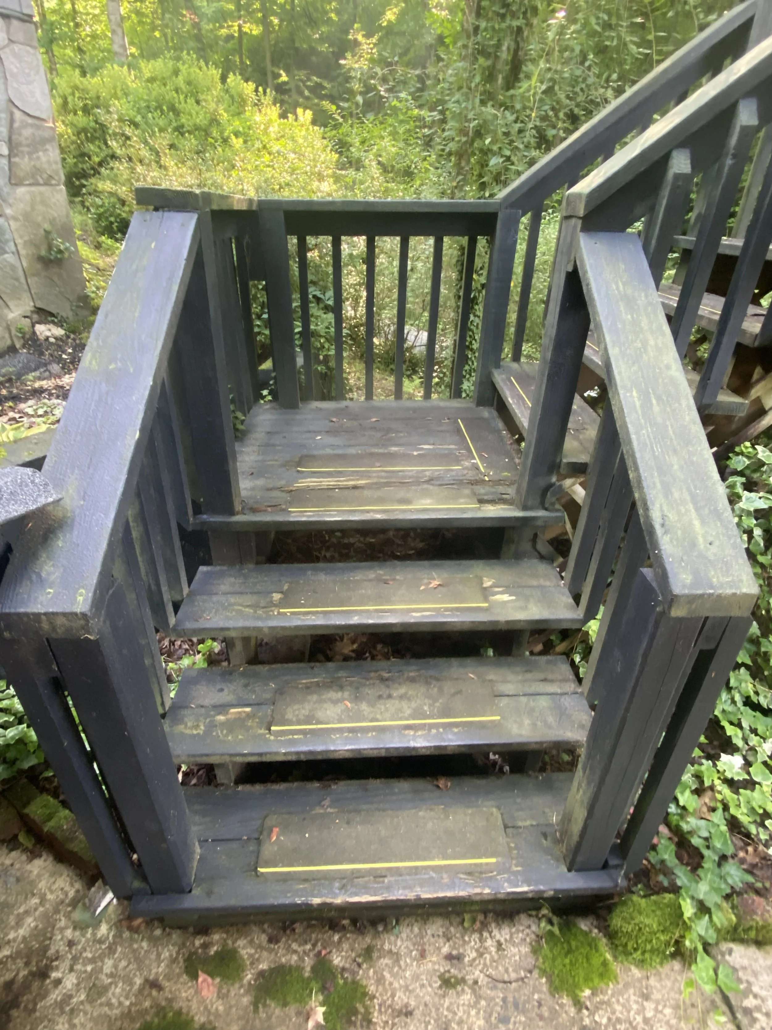 Wooden staircase outdoors, surrounded by green foliage and plants.
