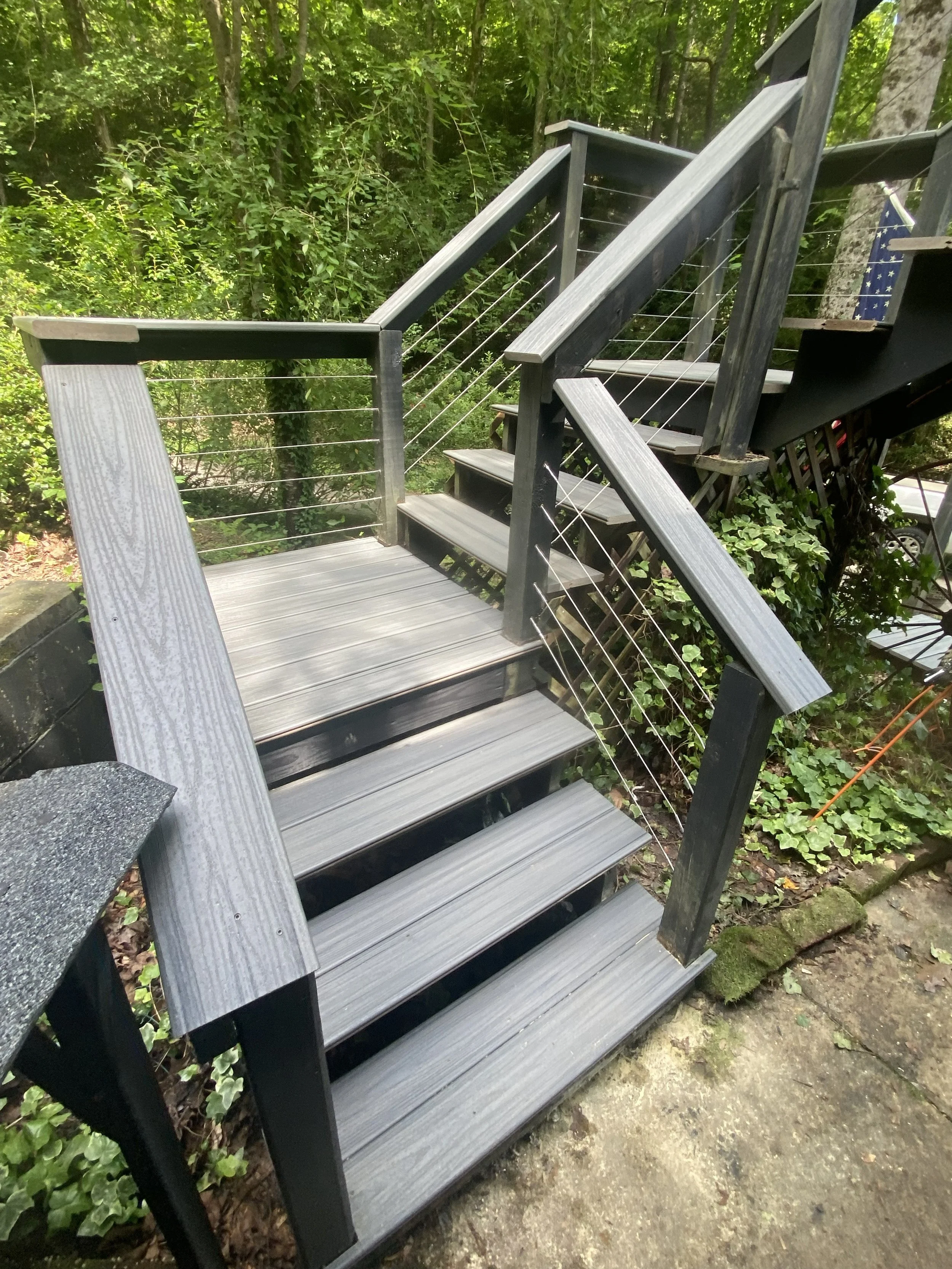 Outdoor staircase with wooden steps and black railings, surrounded by green trees and plants.