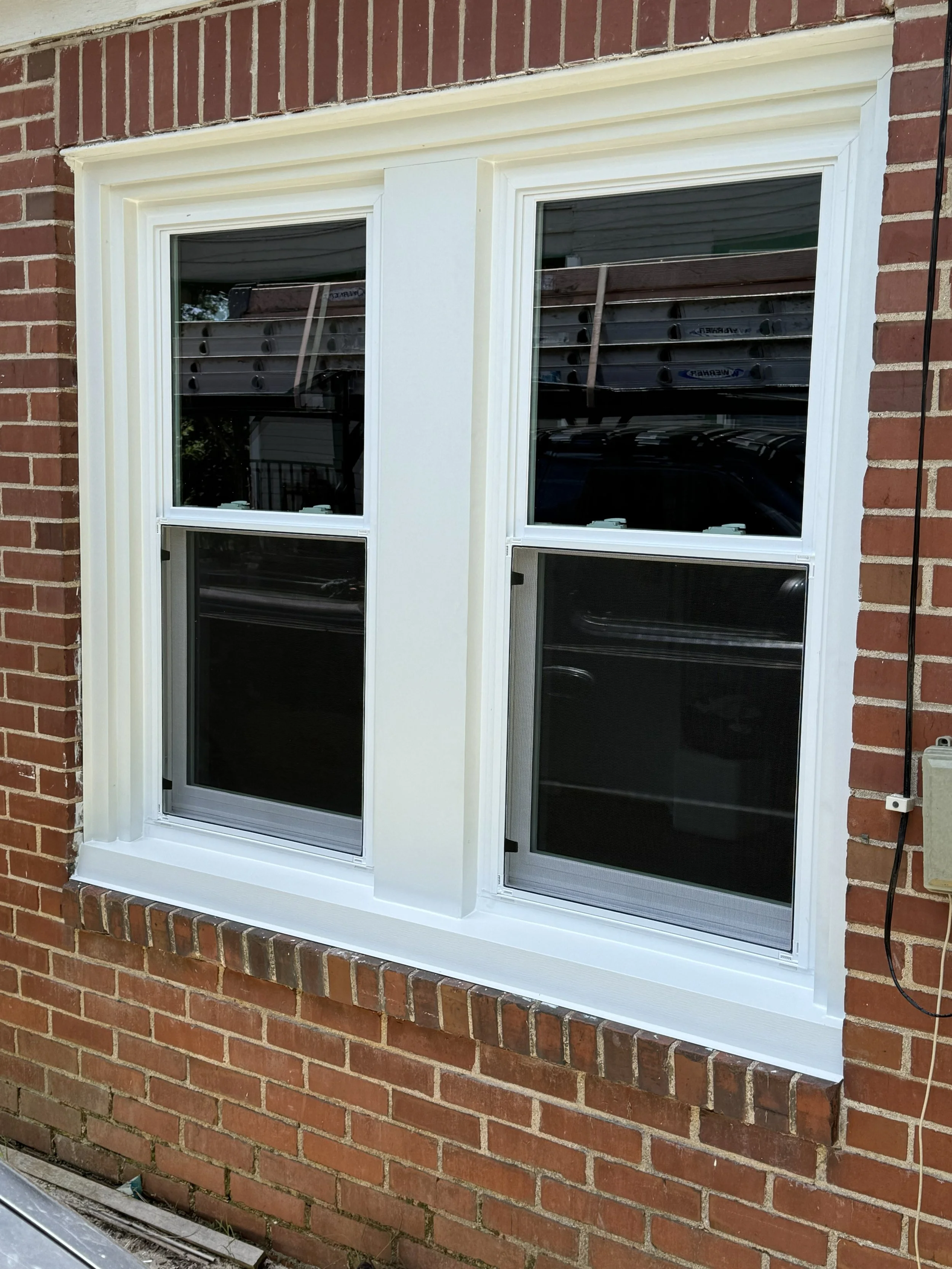 A double-hung window with white trim installed in a red brick wall, with a brick ledge below.