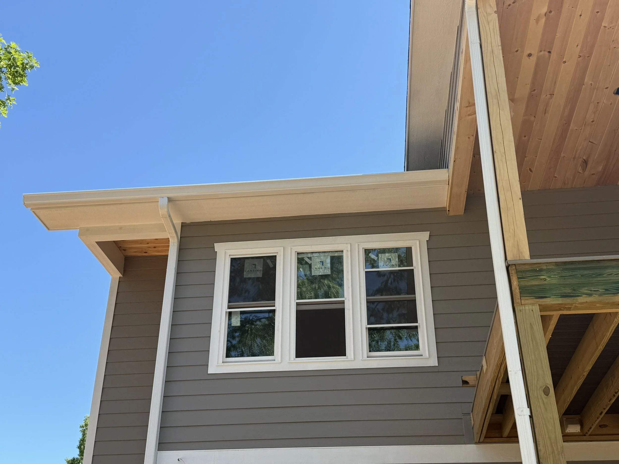 A house with beige siding and white trim, featuring a window with four panes, and a wooden deck with a railing under construction.