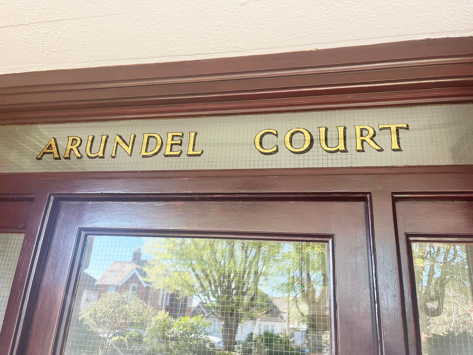 Sign above a wooden door reads 'Arundel Court' in gold letters with black shadowing.