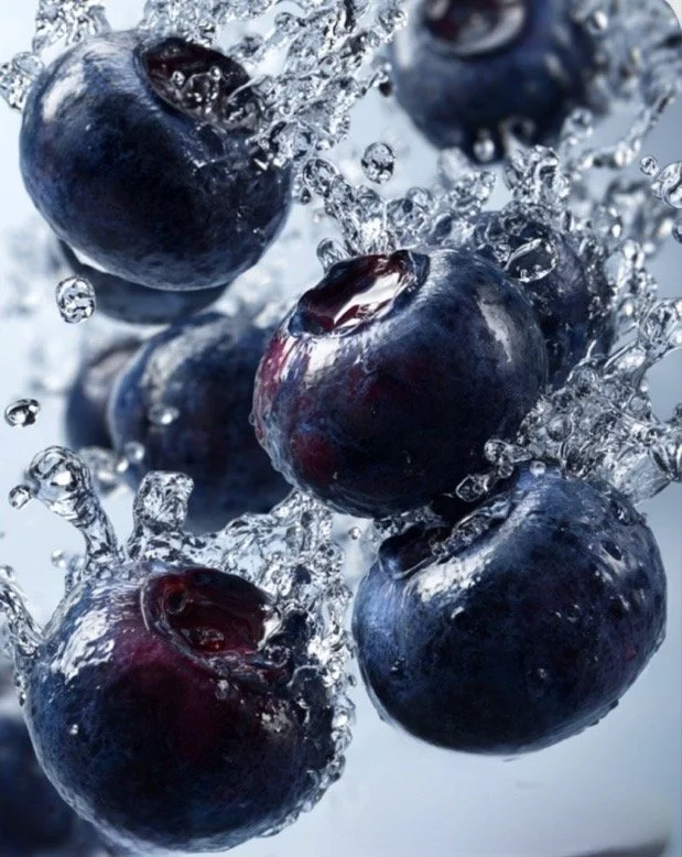Fresh blueberries being dropped into water, creating splash and bubbles.