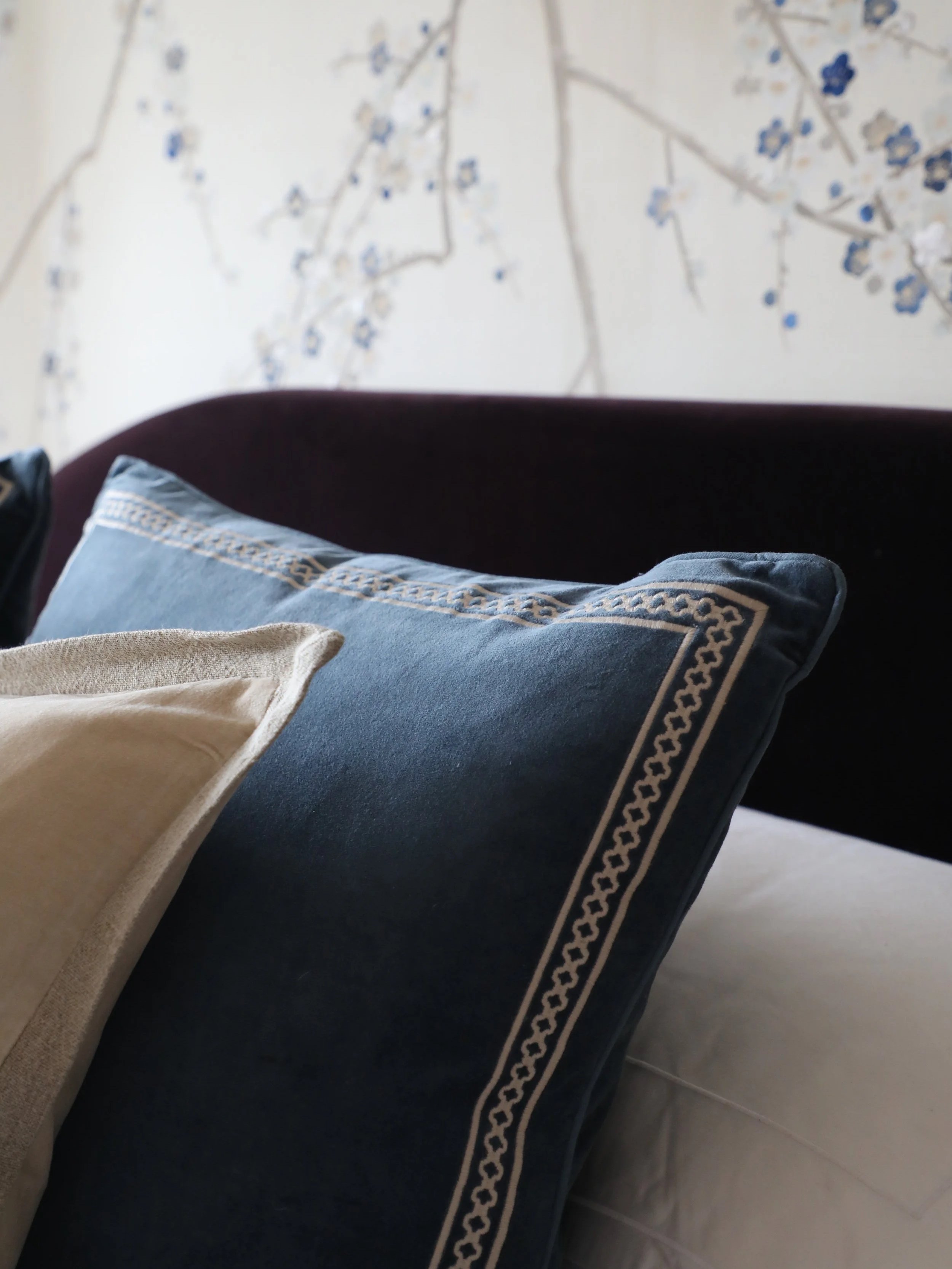 Close-up of a sofa with embroidered cushions in front of a wall with a painted tree with blue and white flowers.