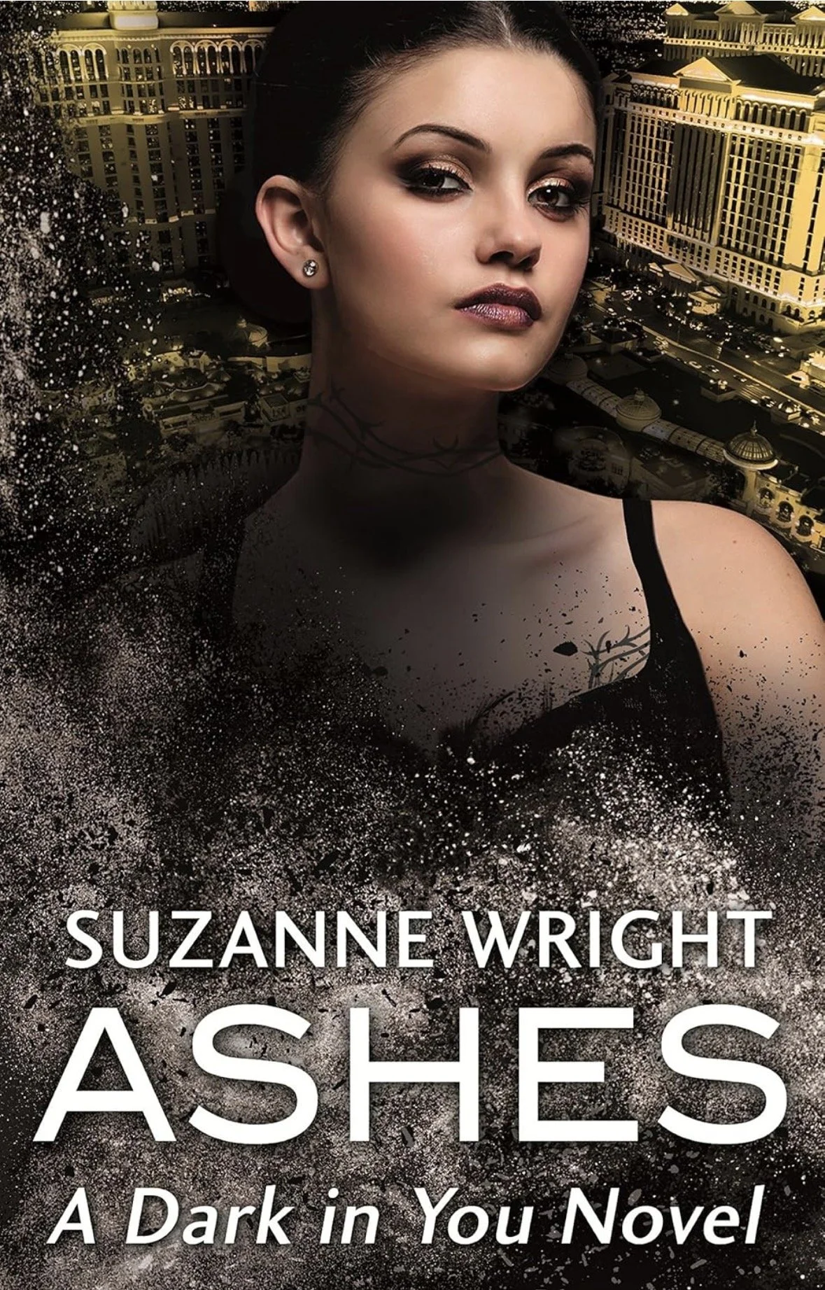 The cover of the book titled 'Ashes' by Suzanne Wright. It features a woman with dark hair, makeup, and earrings, set against a background that combines an urban cityscape with a dark, splattered effect, giving a mysterious and intense vibe. The subtitle reads 'A Dark In You Novel.'