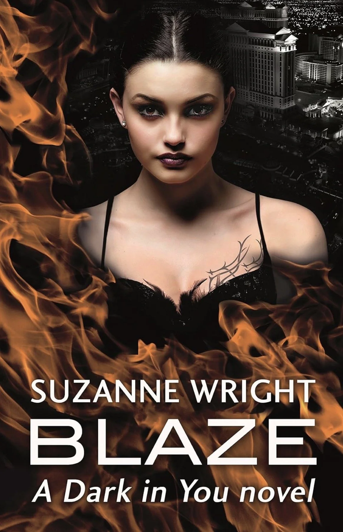Book cover for 'Blaze: A Dark in You novel' by Suzanne Wright, featuring a woman with dark hair, intense makeup, and a tattoo on her shoulder, with a cityscape background and flames in the foreground.