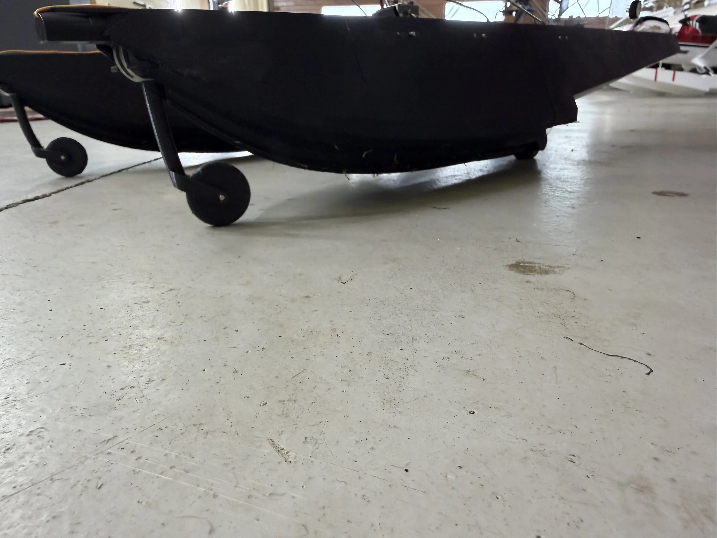 A black kayak with wheels resting on a light-colored concrete floor in an indoor storage area.