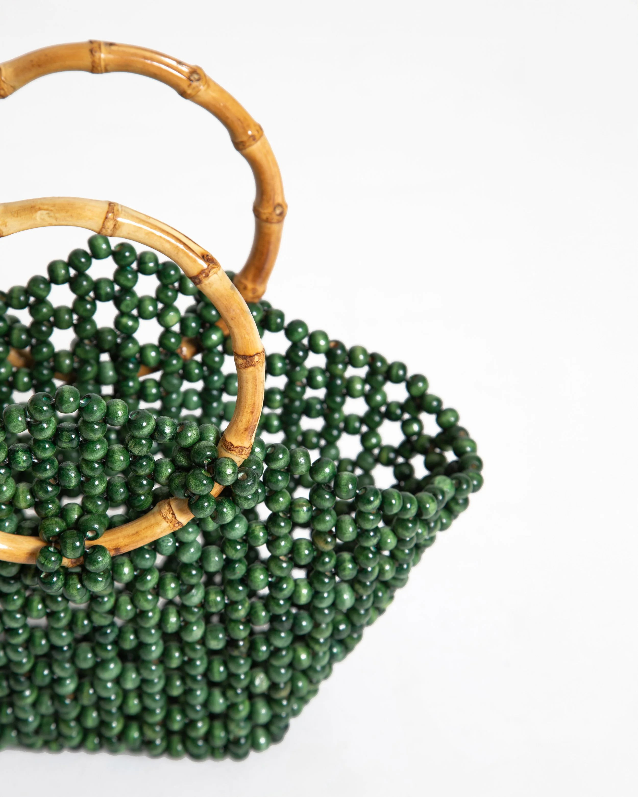 Green beaded purse with bamboo handles on a white background.