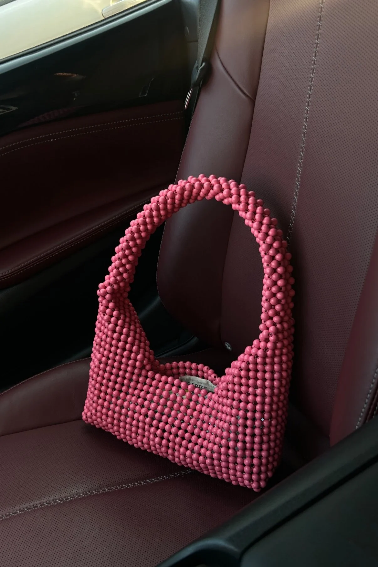 Pink beaded handbag placed on a maroon car seat with leather upholstery.