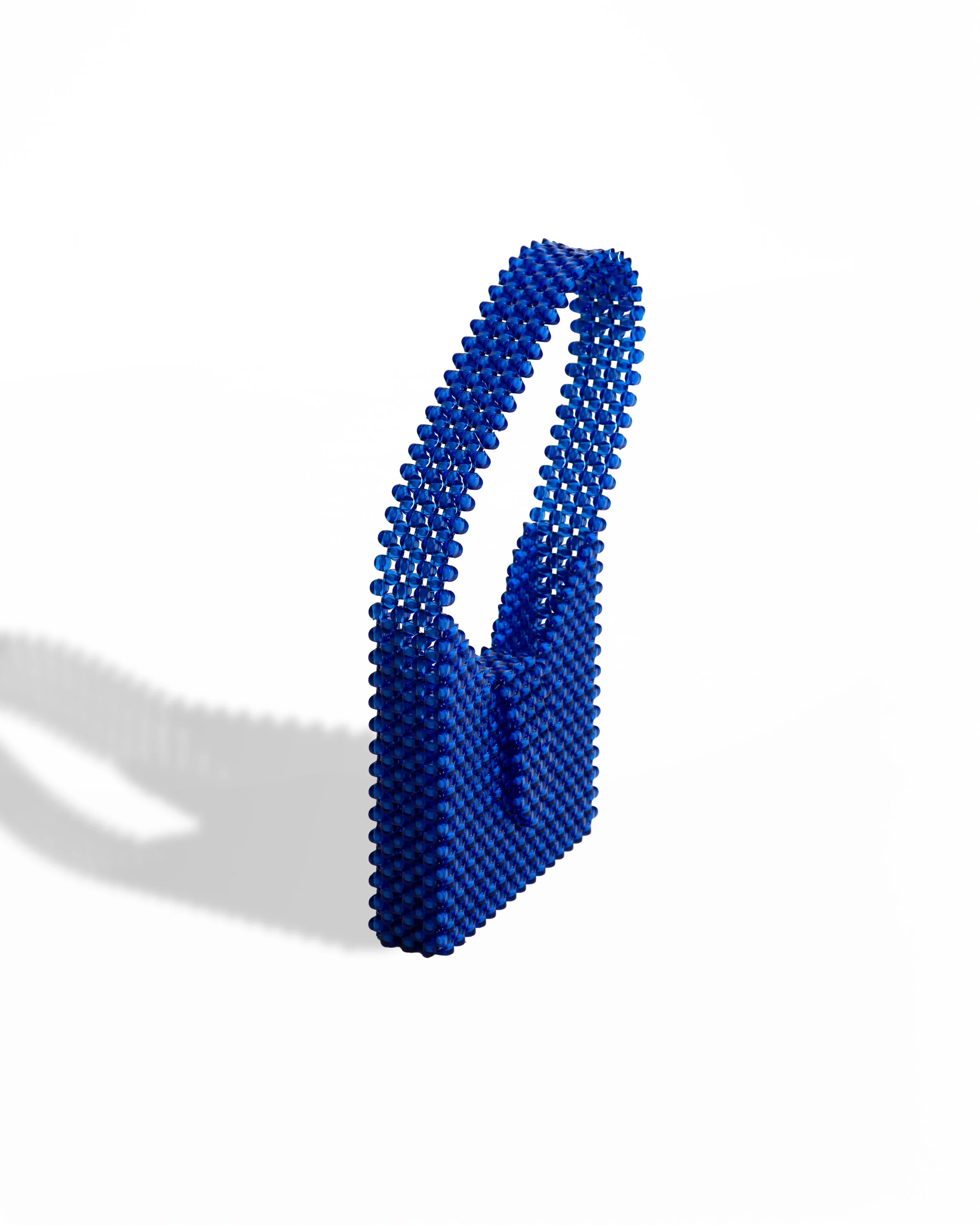 A 3D blue handbag made of small beads with a curved handle, casting a shadow on a white background.