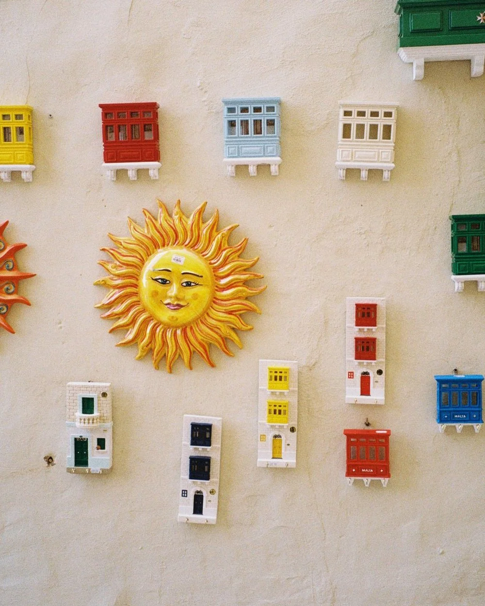 Colorful ceramic sun and miniature mailbox decorations on a wall.